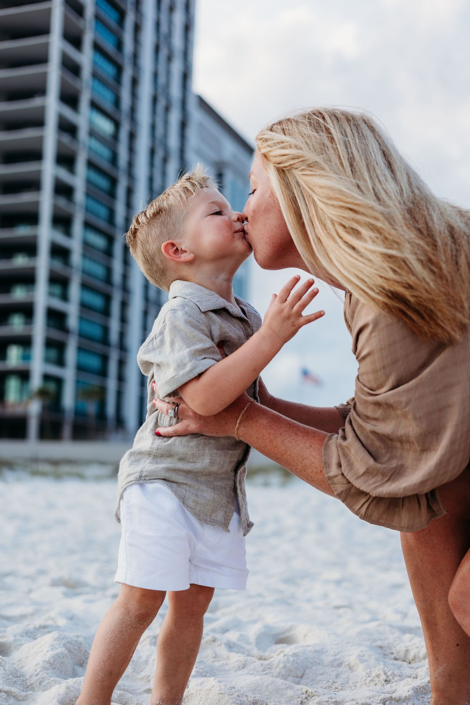 Playful interaction between parent and child on a sandy beach with modern buildings in the background.