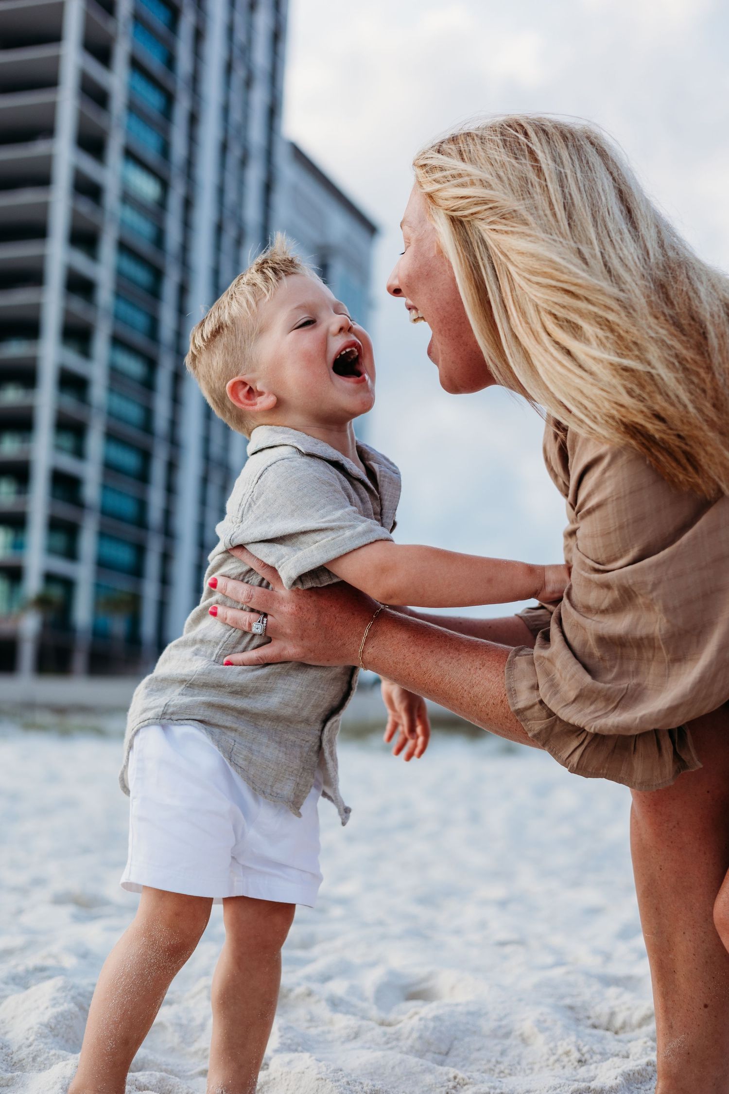 Candid moments of a parent and child playing together on white sand with a city backdrop.