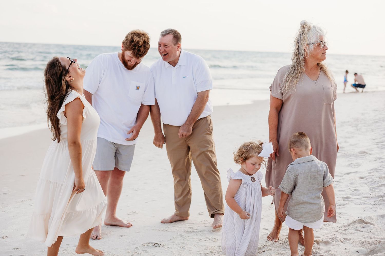 Family members in coordinated neutral outfits enjoy a sunny day at the beach together.