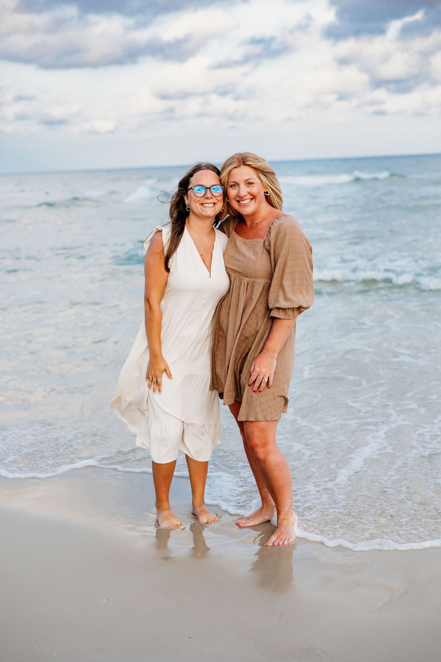 Three people in light colored clothing share joyful moments together at the beach shoreline.