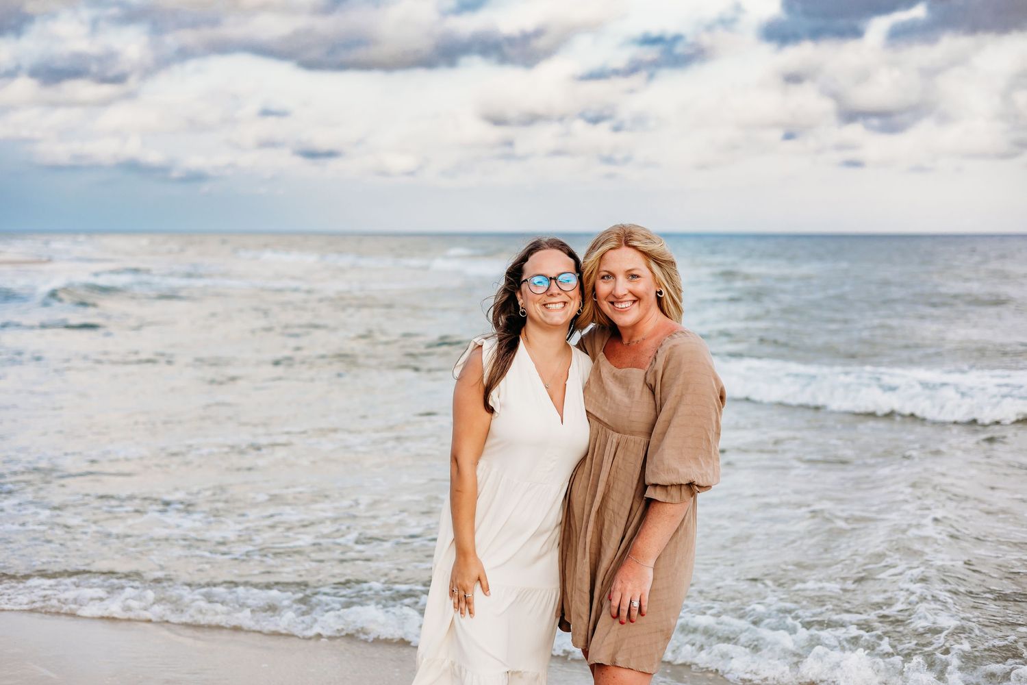 Friends posing together on a beautiful beach with ocean waves and cloudy sky in the background.