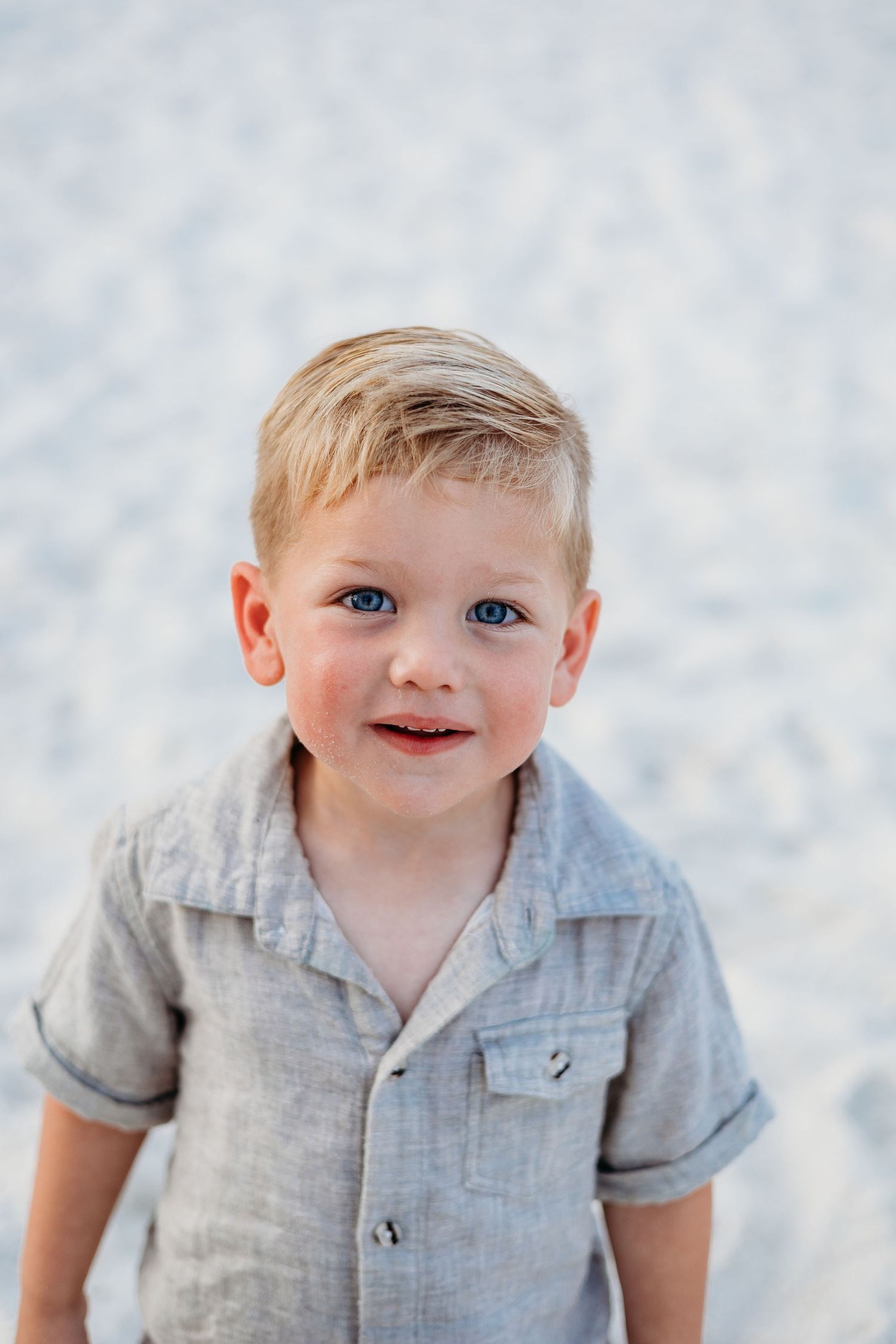 Young child in a gray button-up shirt smiling against a light background.