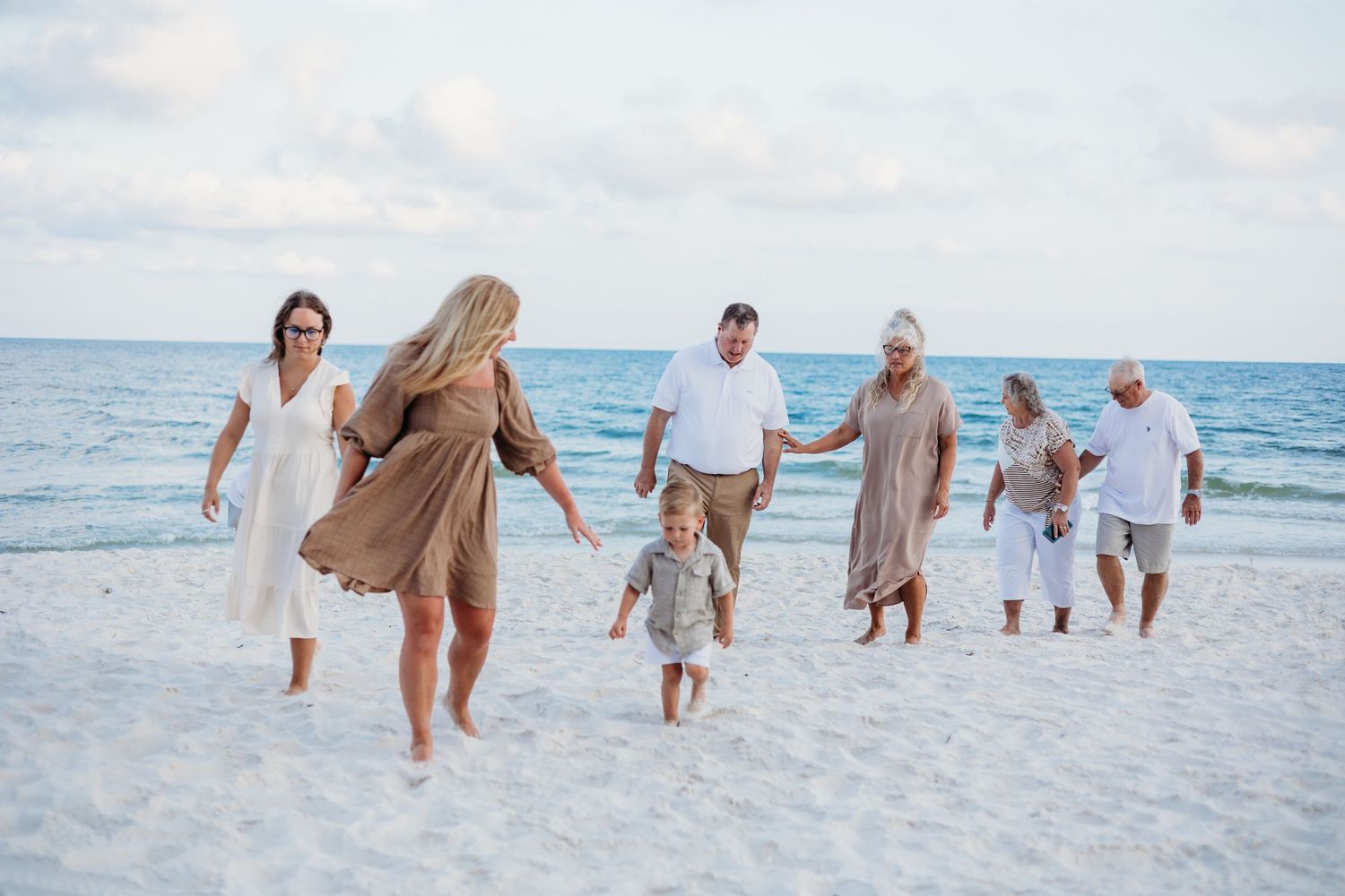 Family group walking and playing together on white sandy beach at sunset.