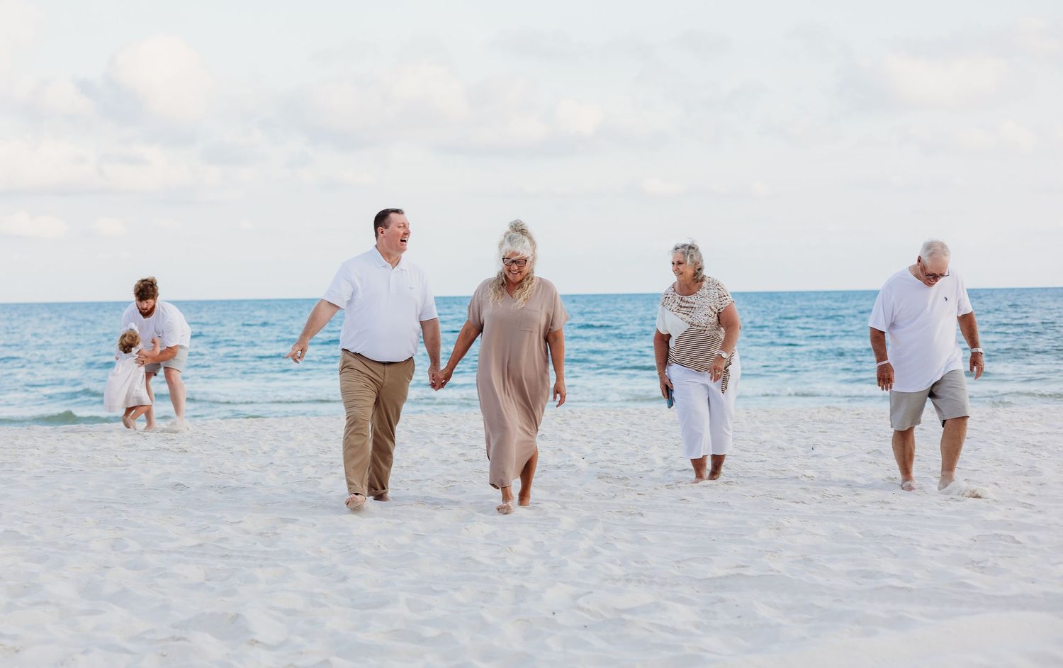 Family members strolling together on white sandy beach with beautiful blue ocean backdrop.