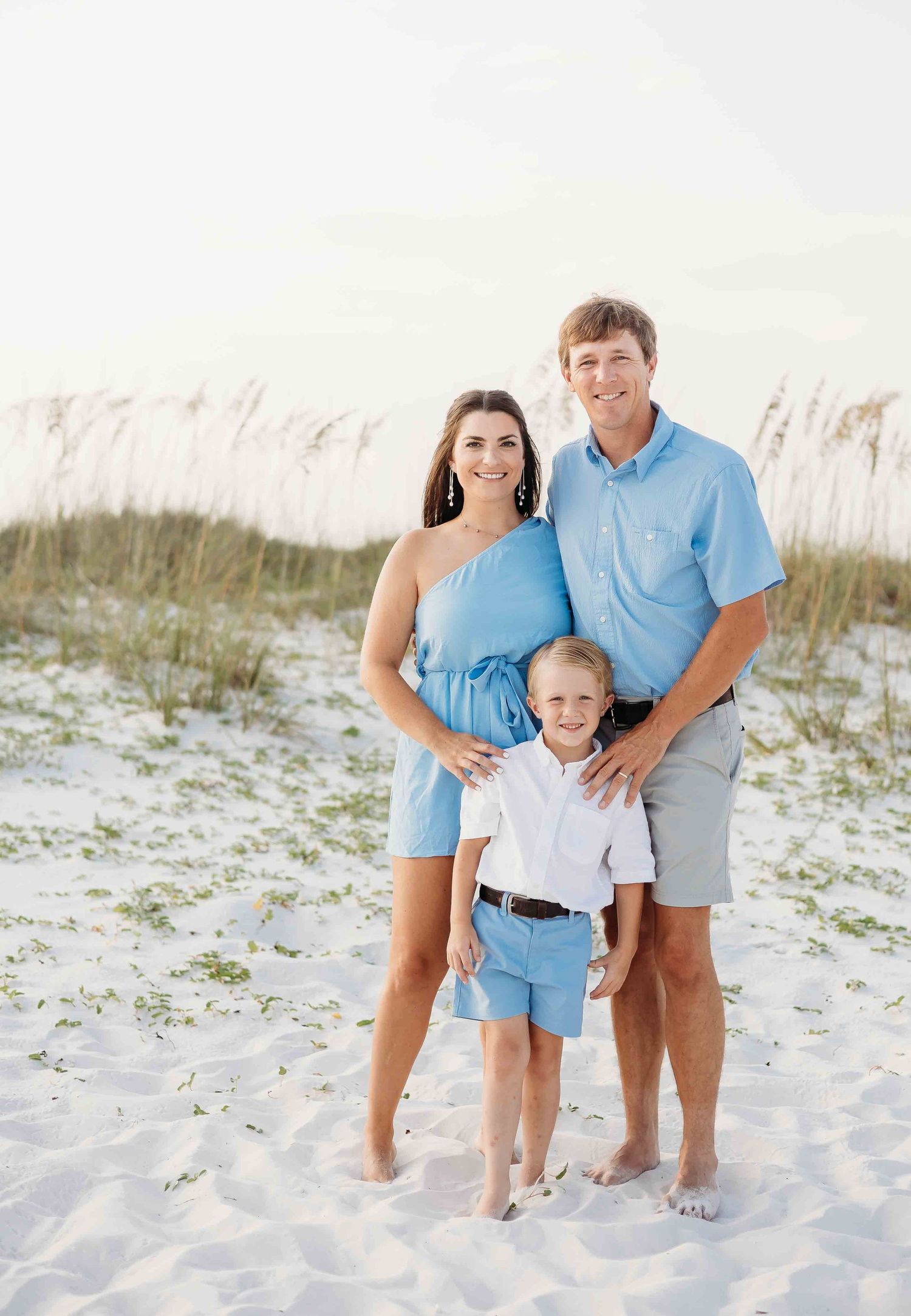 Family in matching blue and white outfits poses together on white sand dunes.