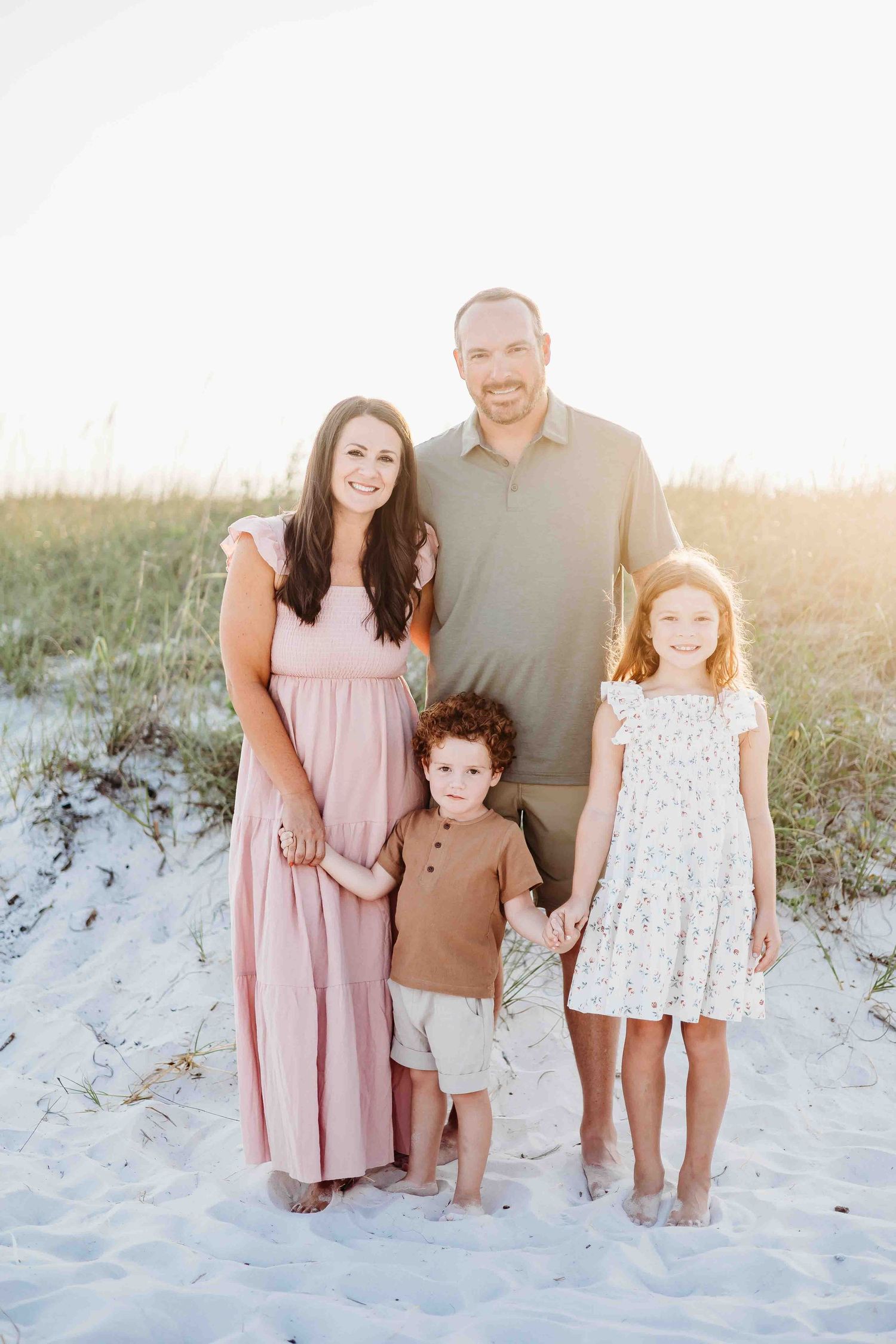 A family poses together on white sand beach during golden hour.