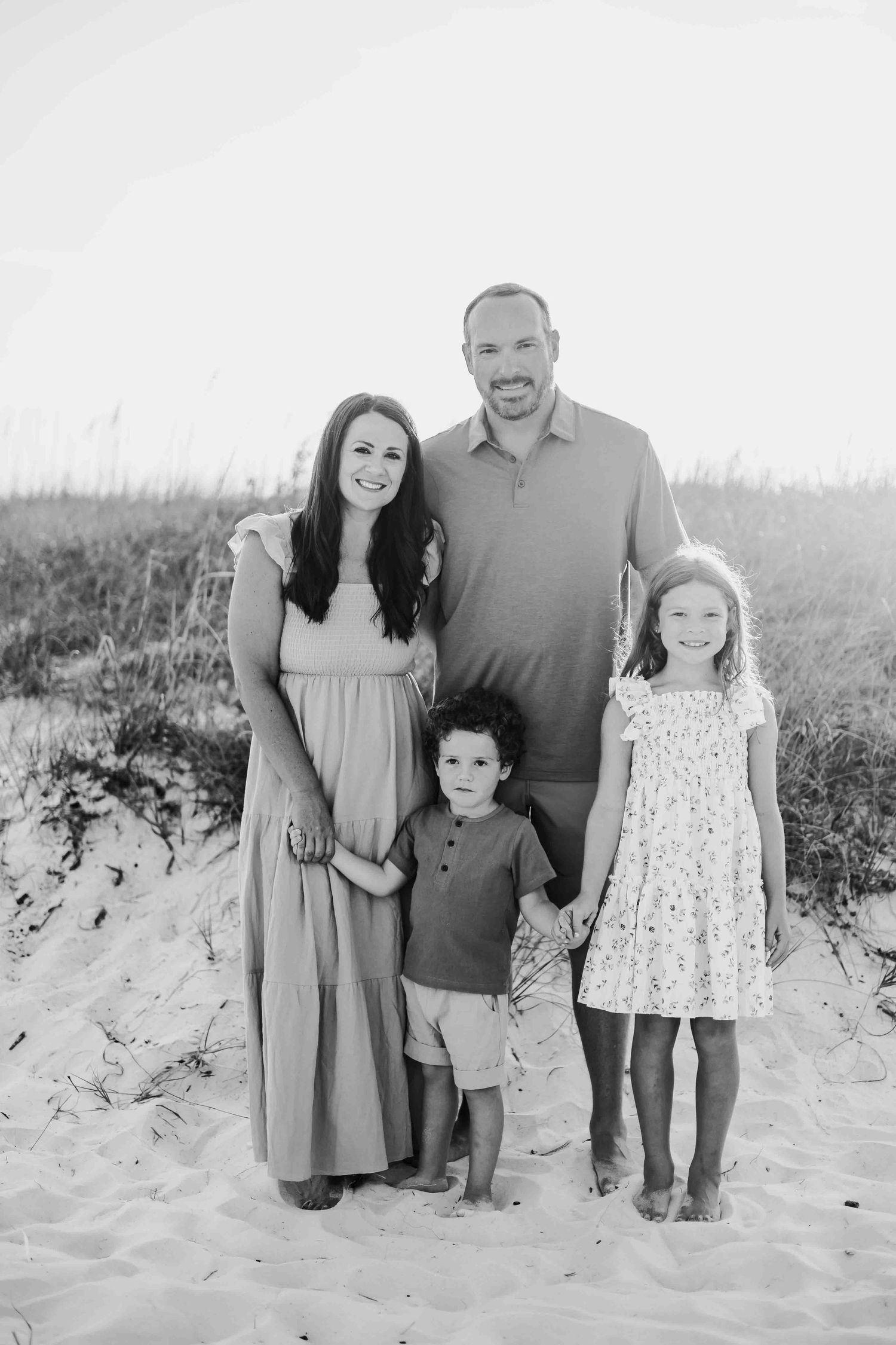 A family wearing coordinated outfits poses together on a sandy beach at sunset.
