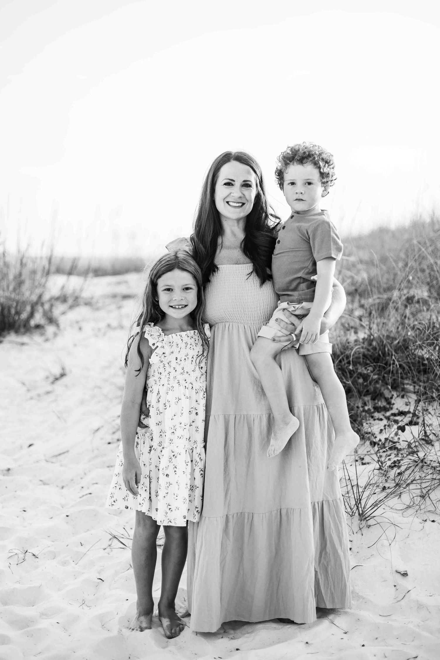 Family members in coordinated gray and pink outfits stand together on white sand dunes.