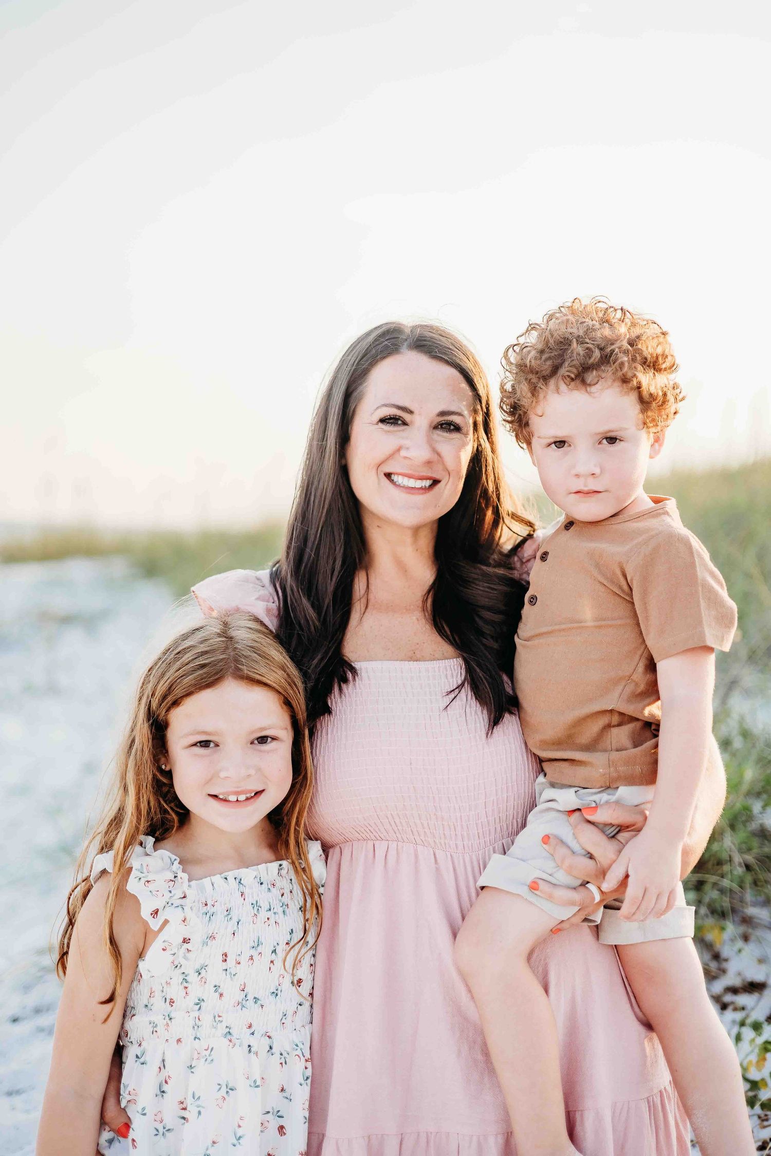 A sweet beach portrait of family members wearing pink and floral outfits against white sand.