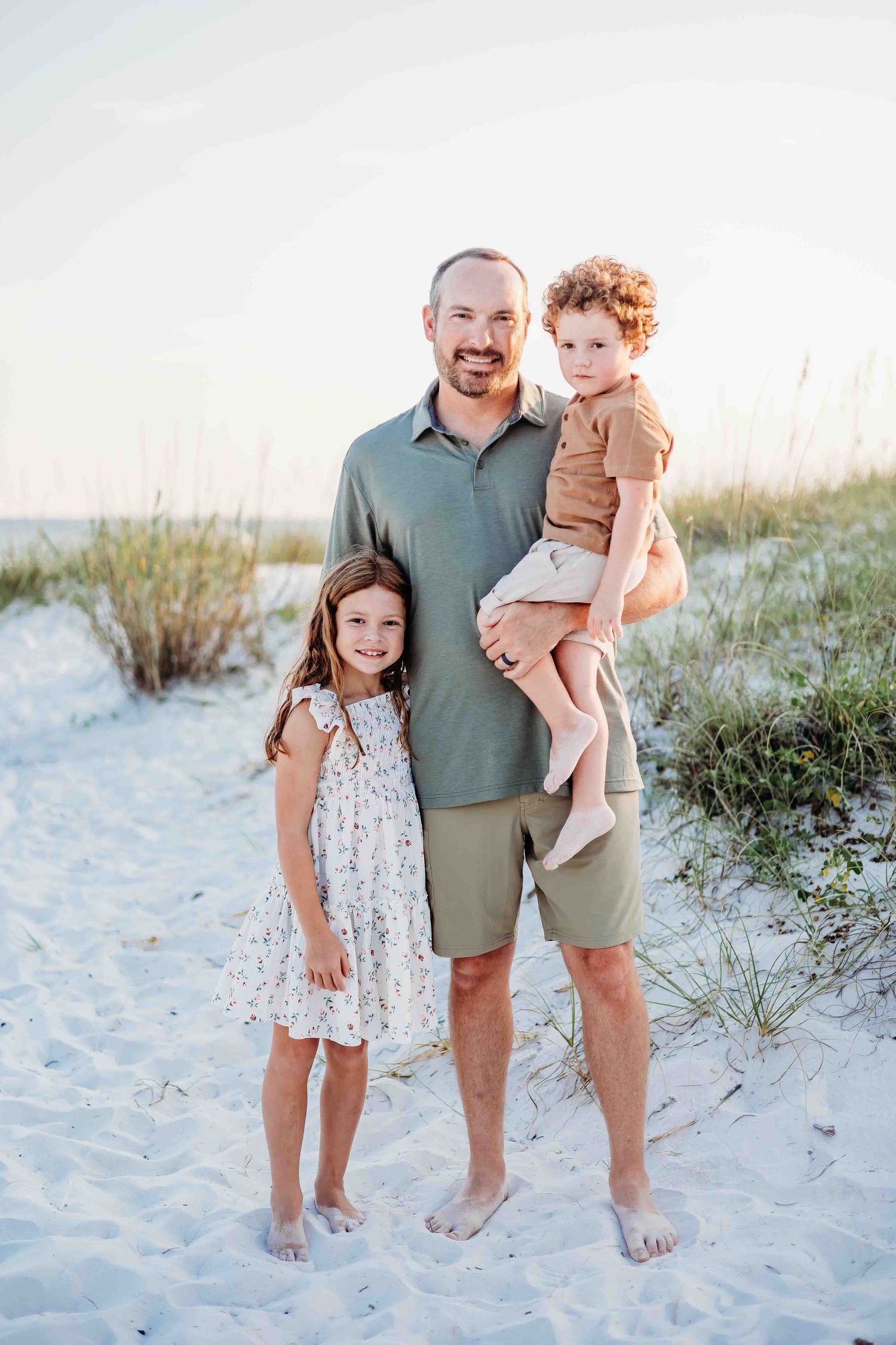Casual family beach portraits with members wearing coordinated outfits on sandy dunes.