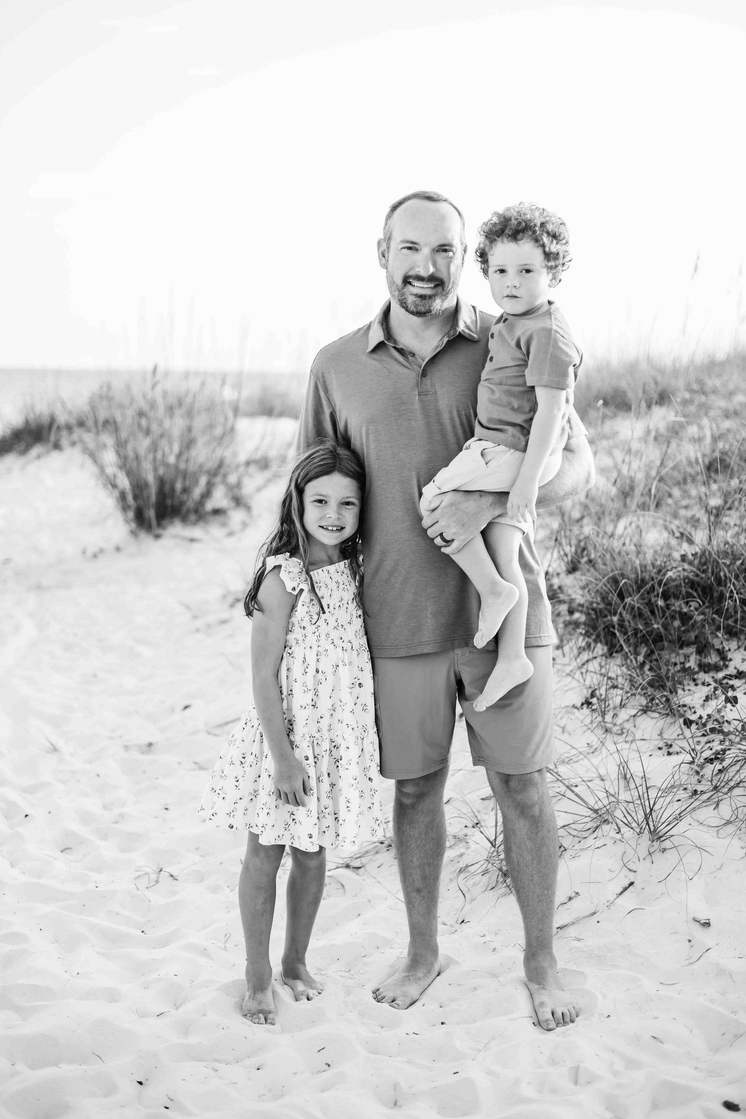 Black and white family portrait on a sandy beach with dune grass in the background.