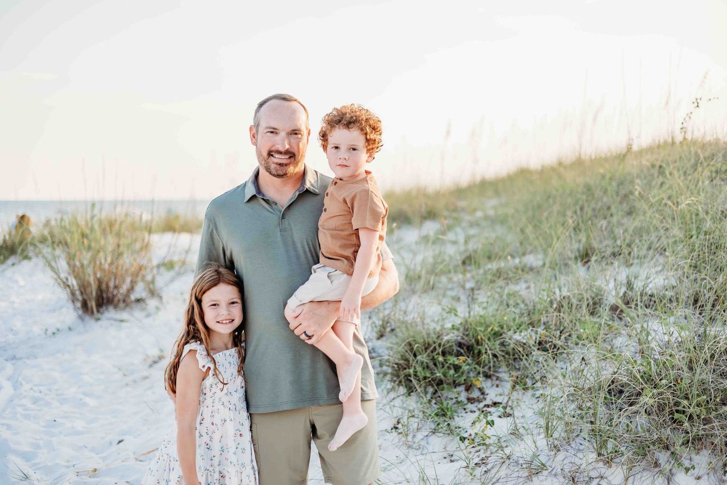 Family members stand barefoot together on white sand during a beach photo session.