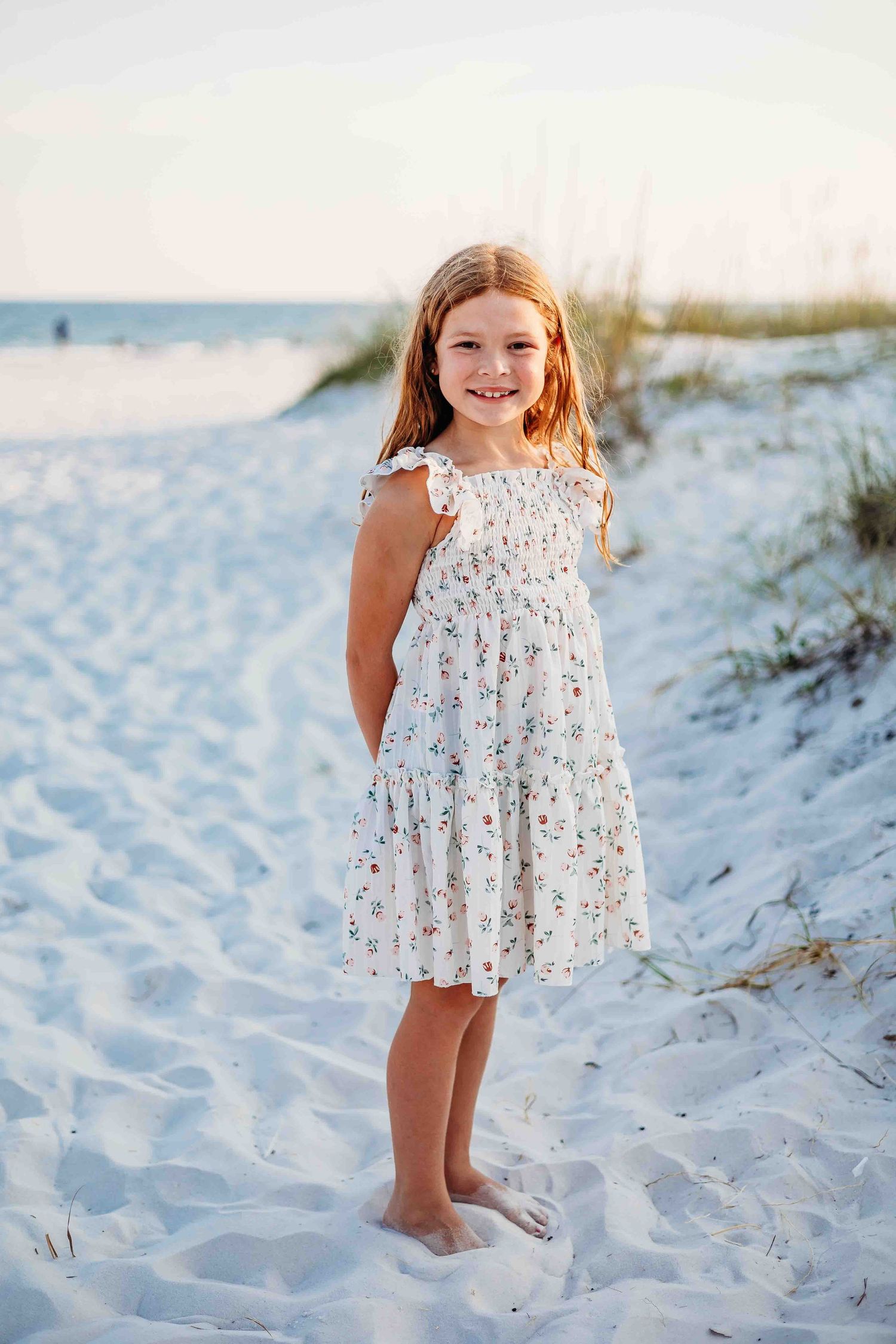 A white floral dress stands out against pristine beach sand during golden hour.