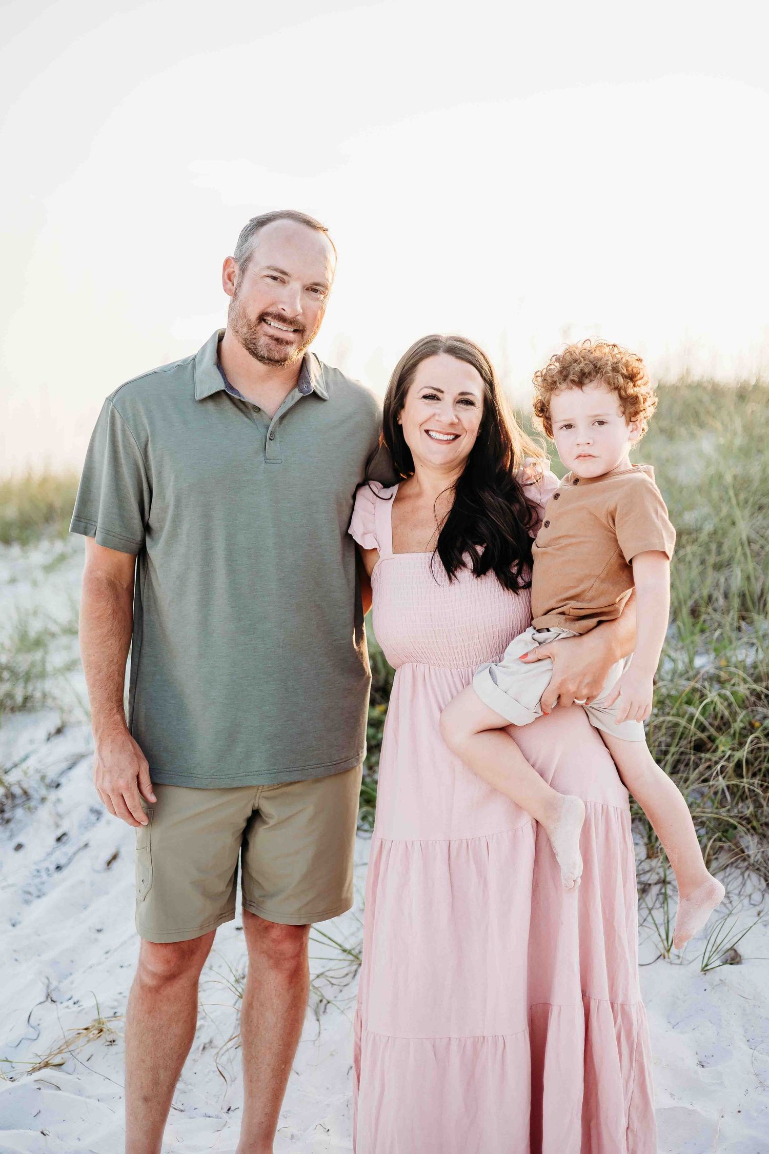 Family wearing coordinated pink and green outfits poses together on white sand beach.