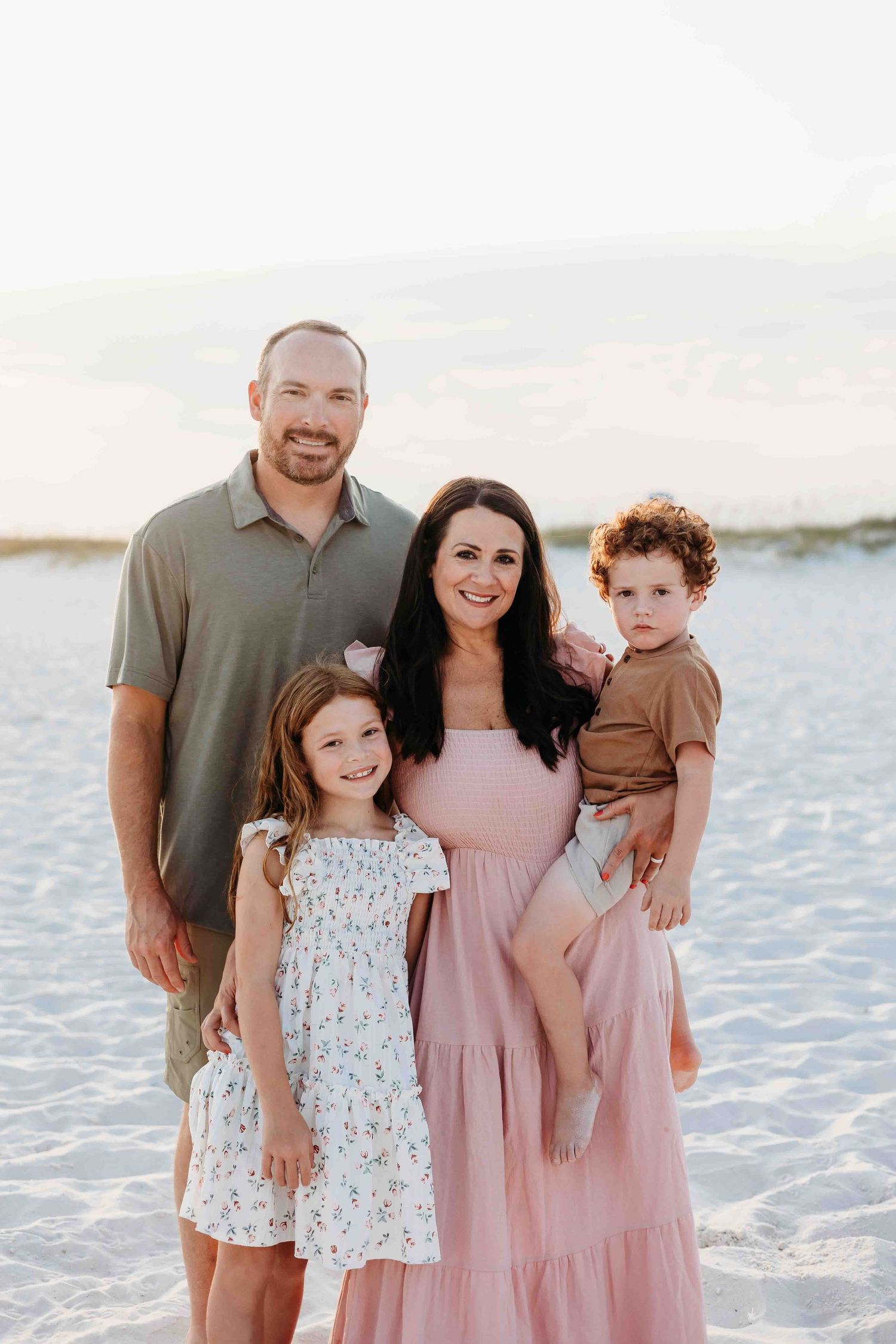 Family portrait on beach with parents and children wearing pink and floral dresses.