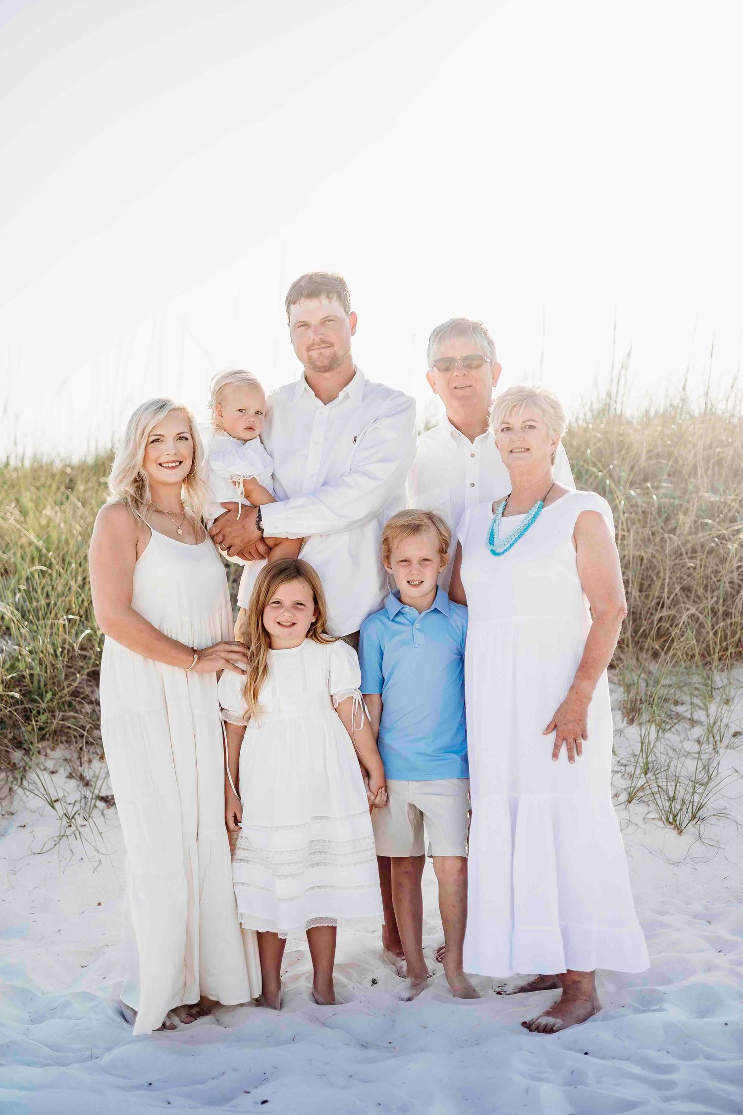 Extended family gathering on sandy beach wearing white and blue casual clothing.