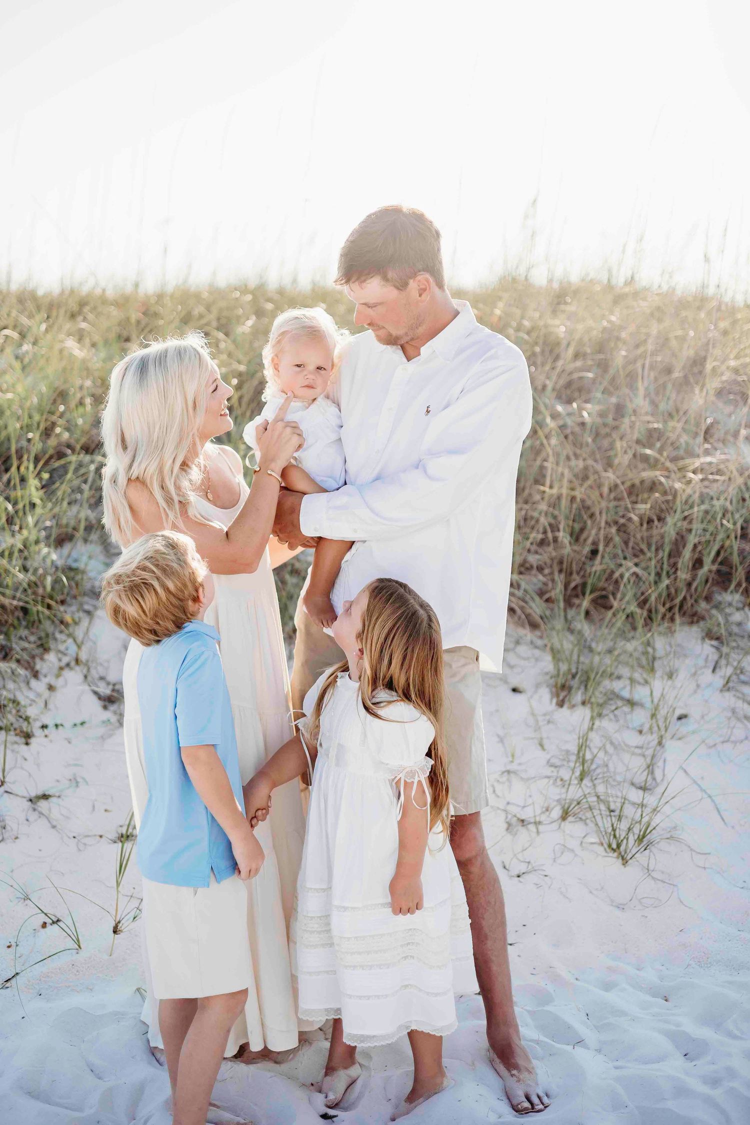 Playful family interaction on beach dunes wearing coordinated summer clothing.