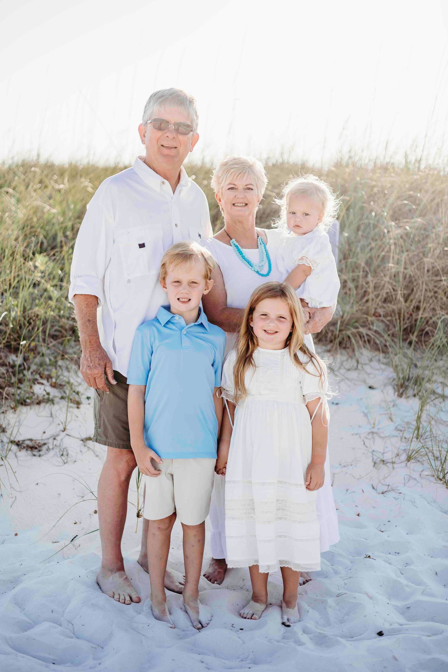 A family portrait on a sunny beach with white sand and beach grass in the background.