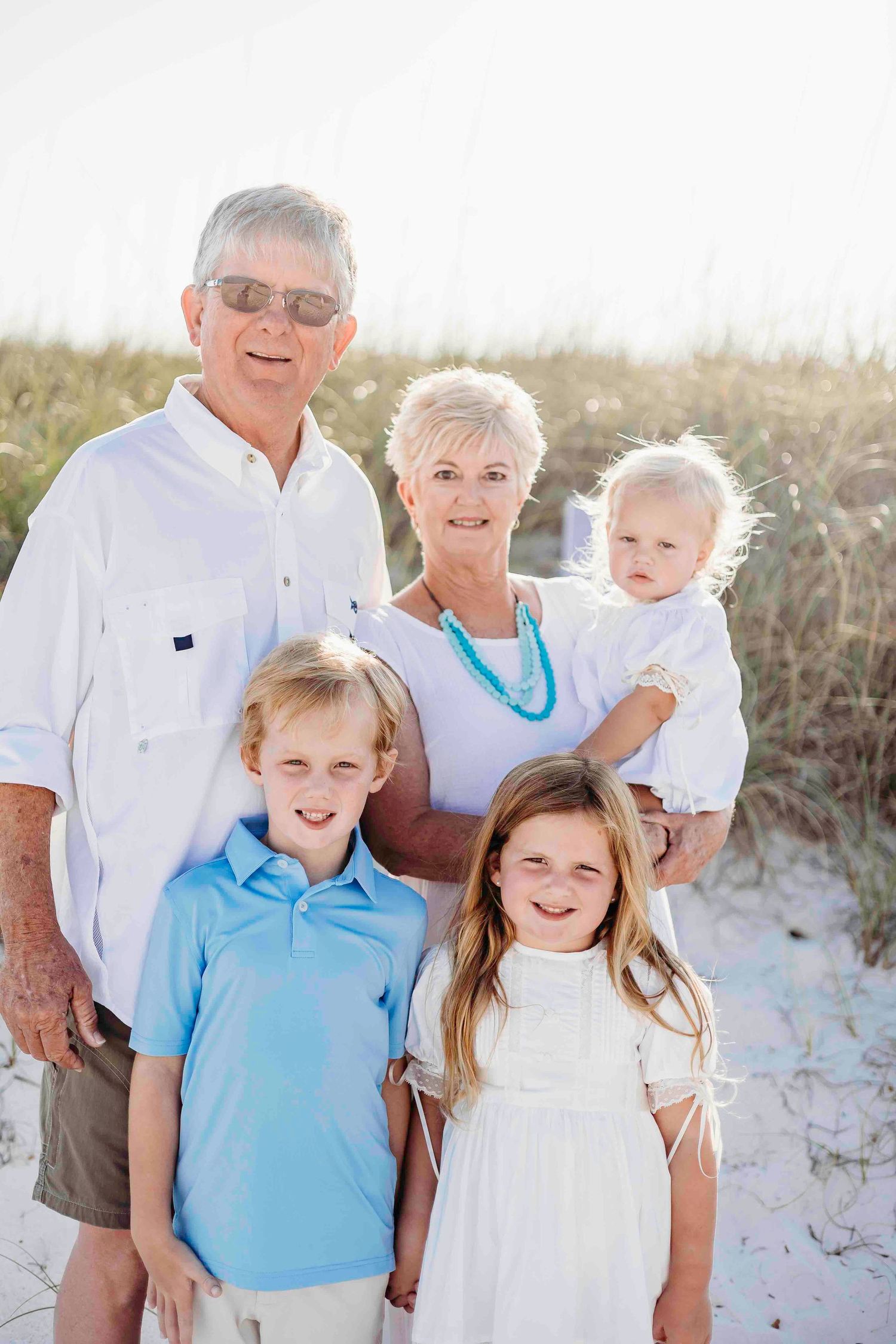 Multi-generational family wearing blue and white outfits posing together on a sandy beach.