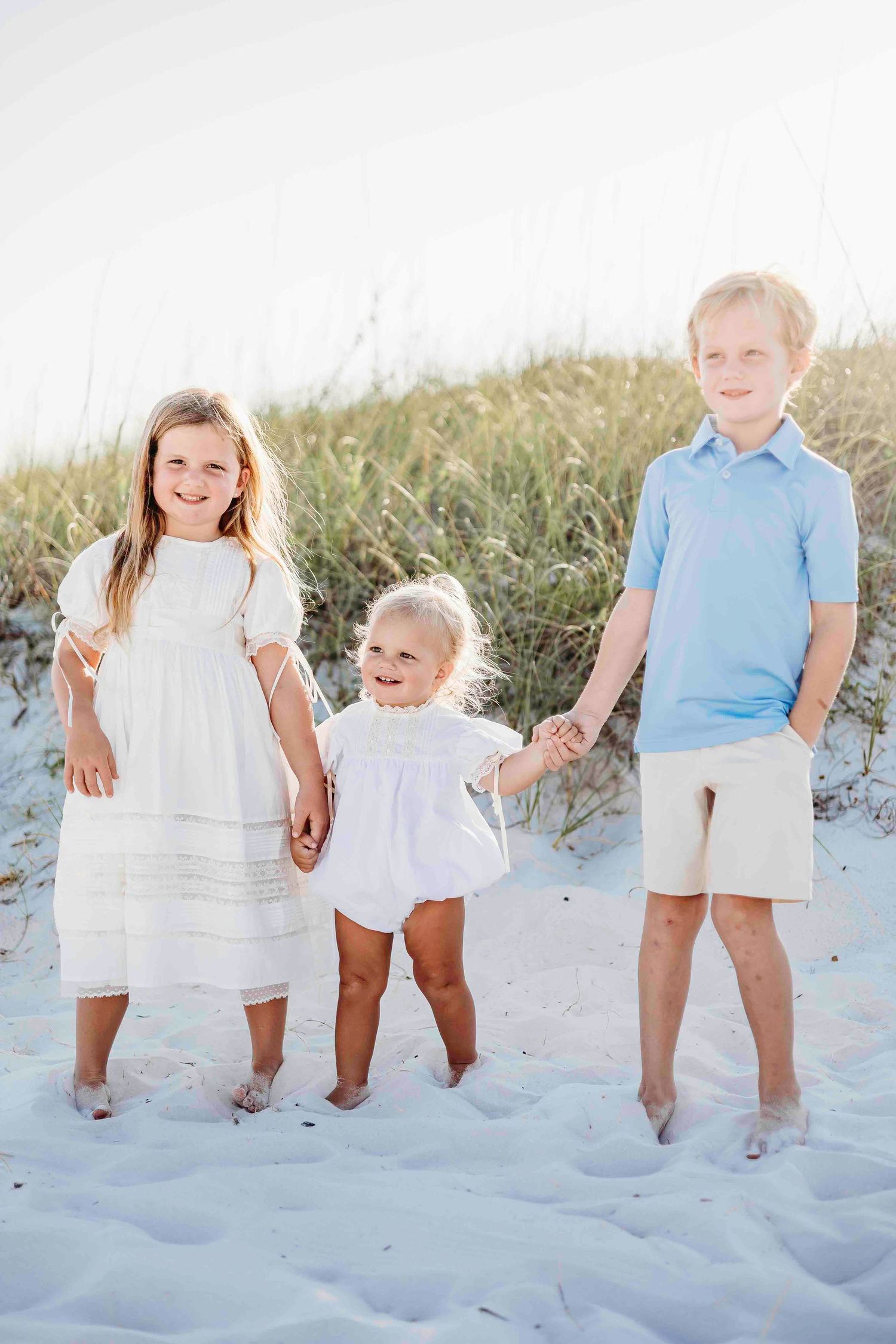 Kids lined up on beach sand wearing coordinated summer outfits in white and blue.