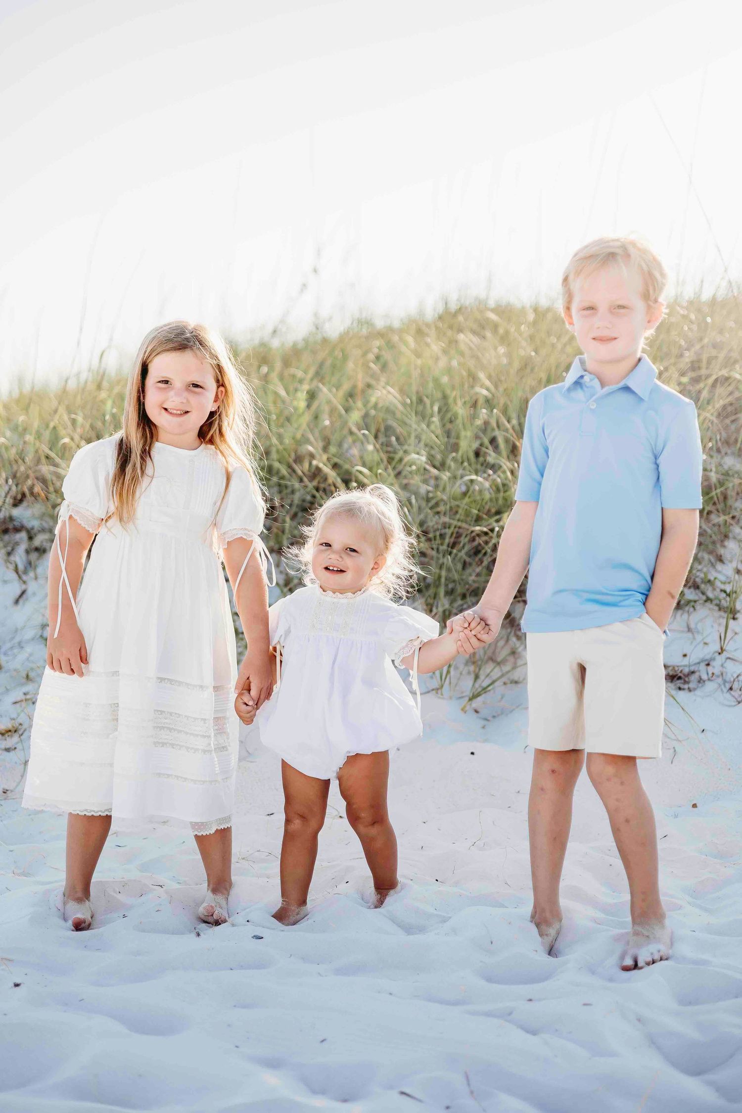 Group of children standing together on sandy beach wearing matching white and blue outfits.