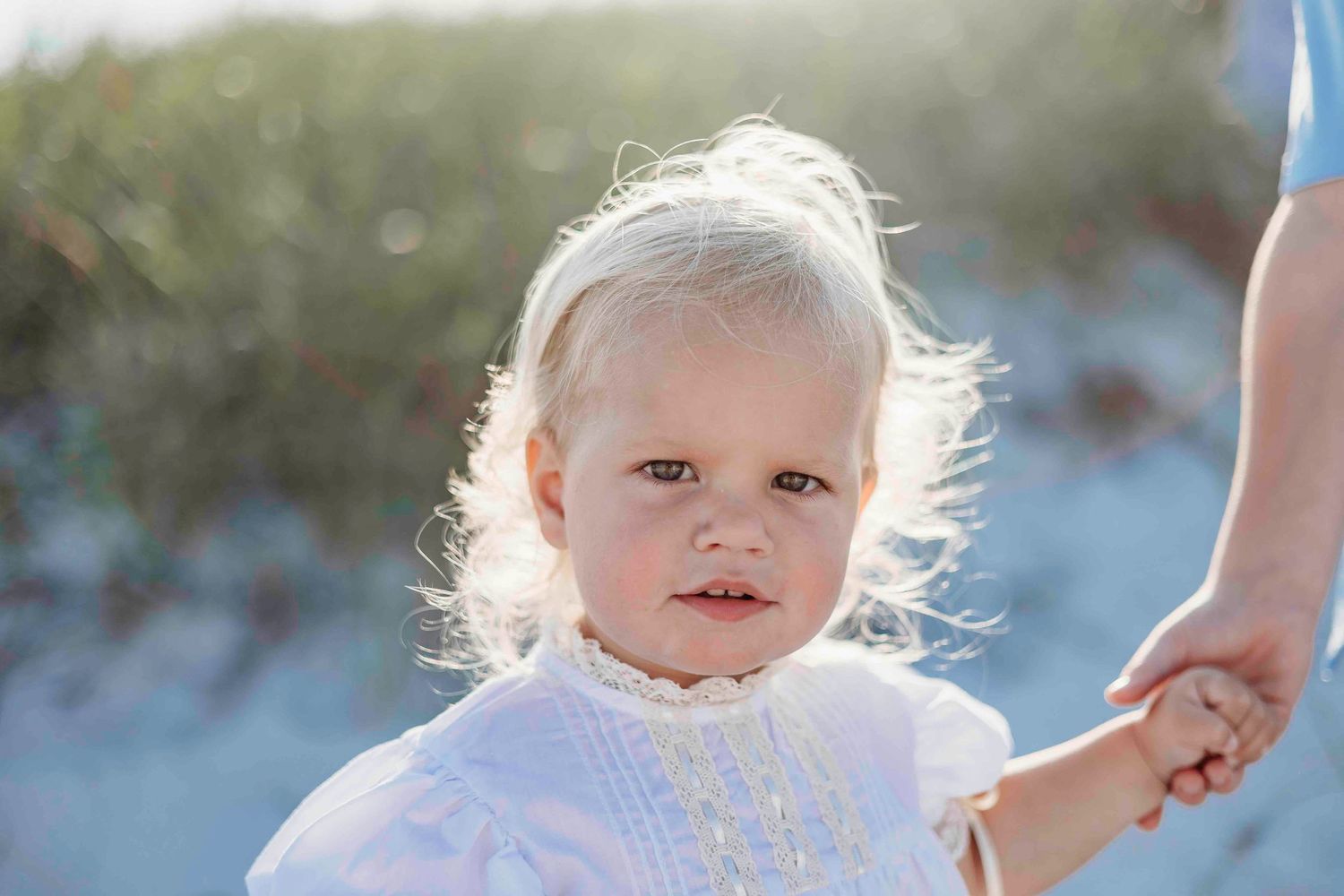 A young child wearing a white dress plays on a sandy beach during a sunny day.