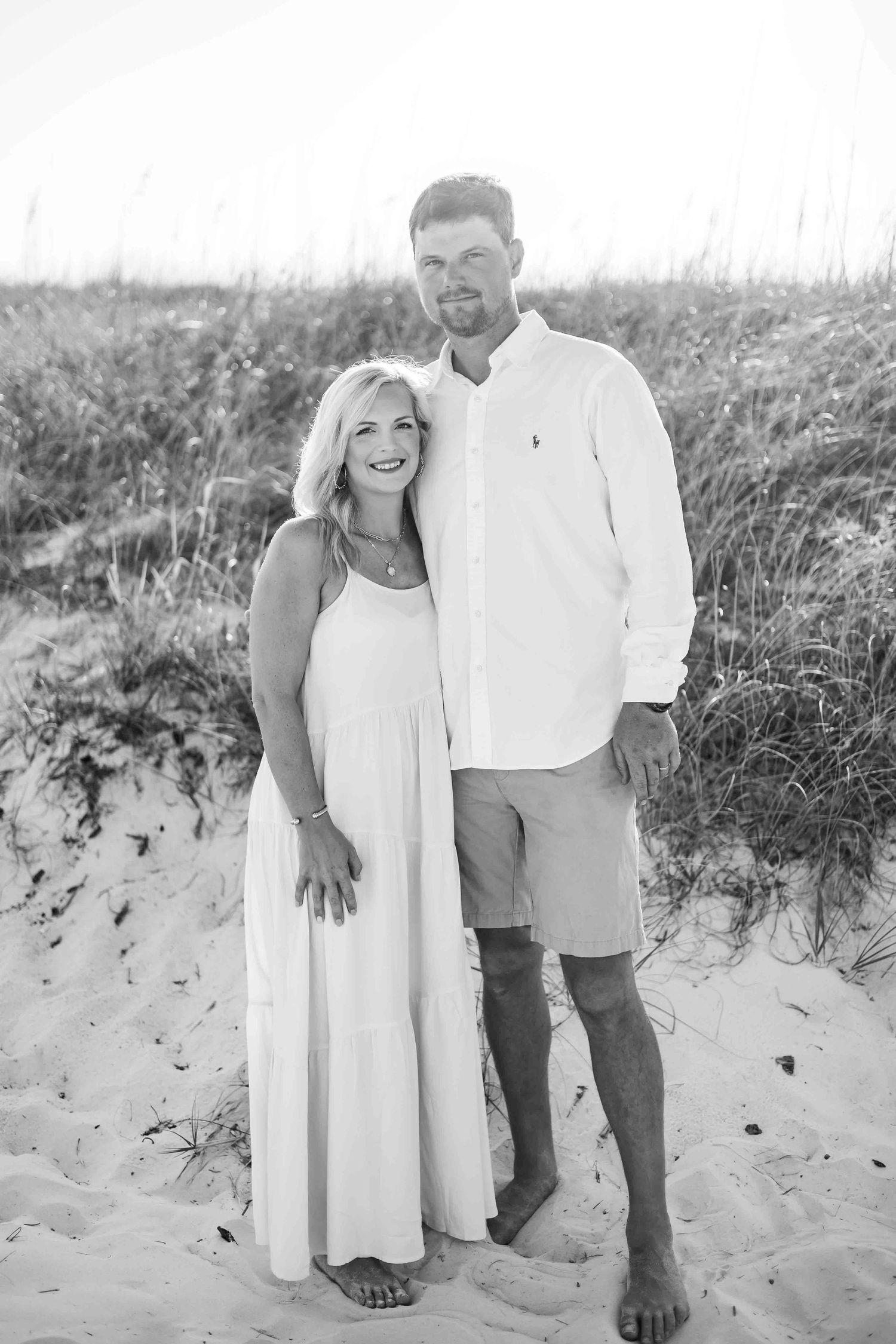 Black and white portrait of couple embracing on beach dunes.
