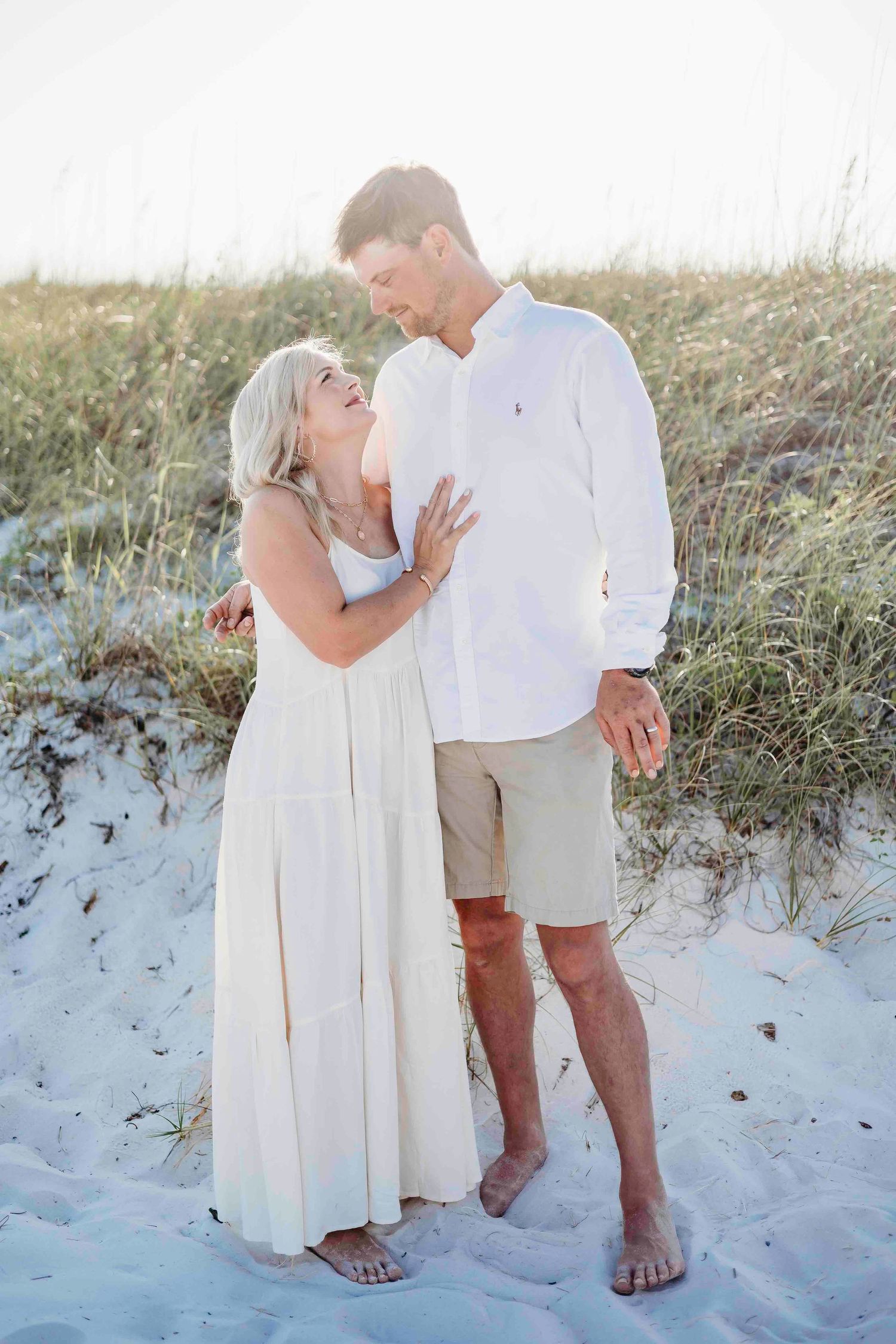 Joyful couple laughing together while standing on sandy beach during sunset.
