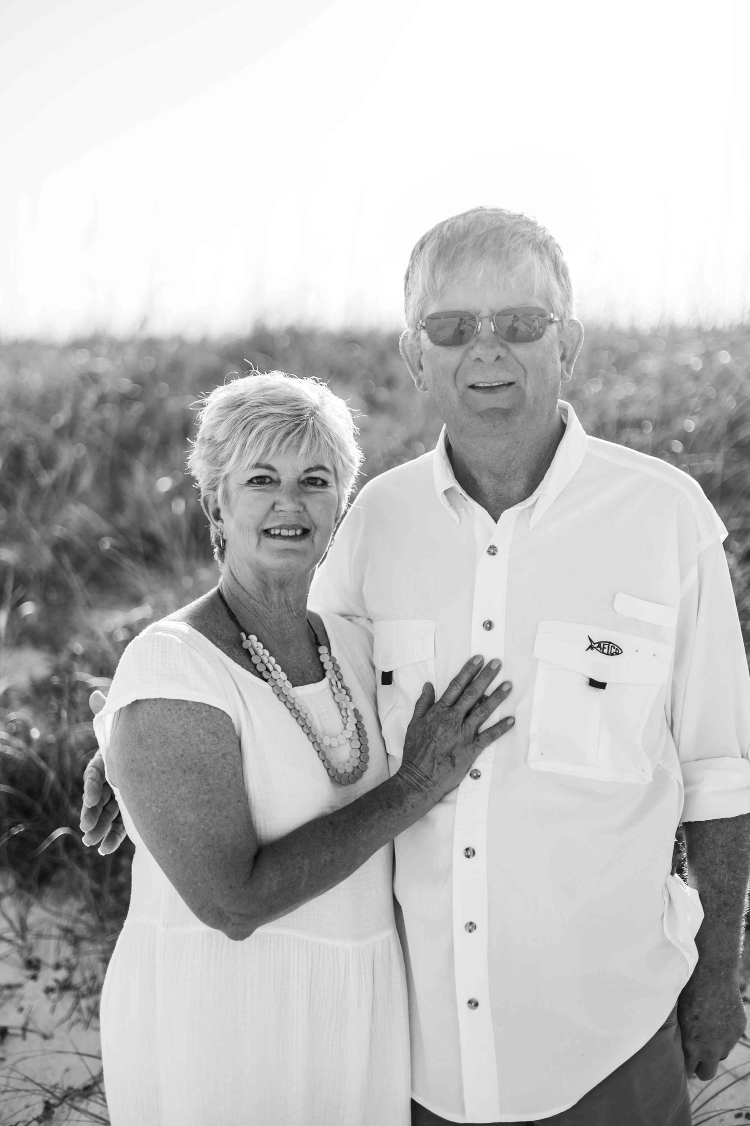 Black and white portrait of senior couple in white attire on beach dunes.