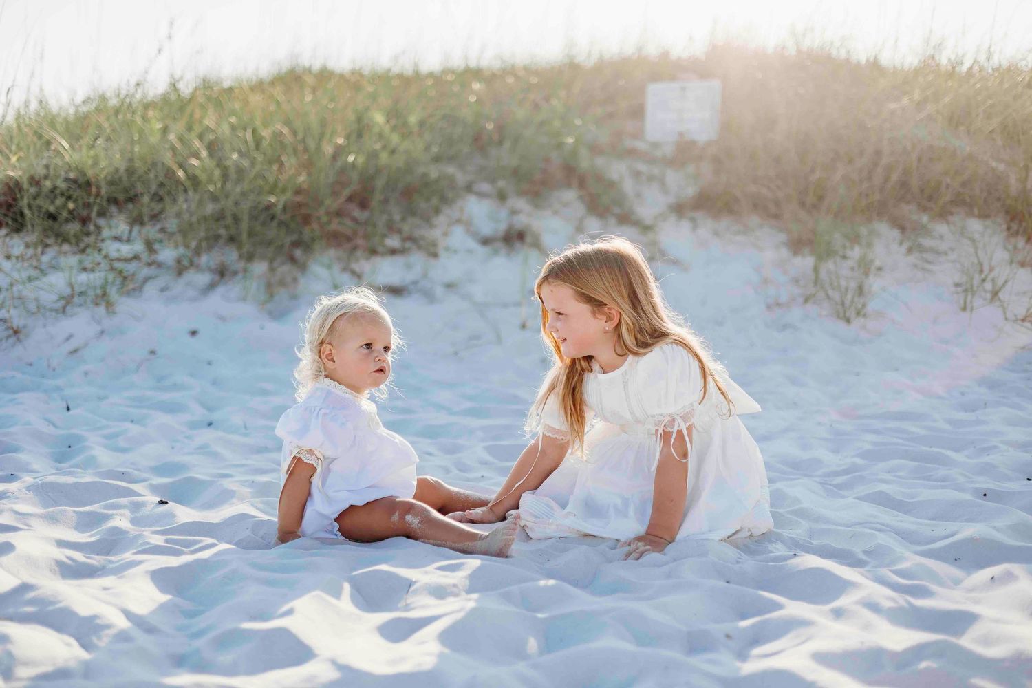 Children play together on white sandy beach during golden hour.