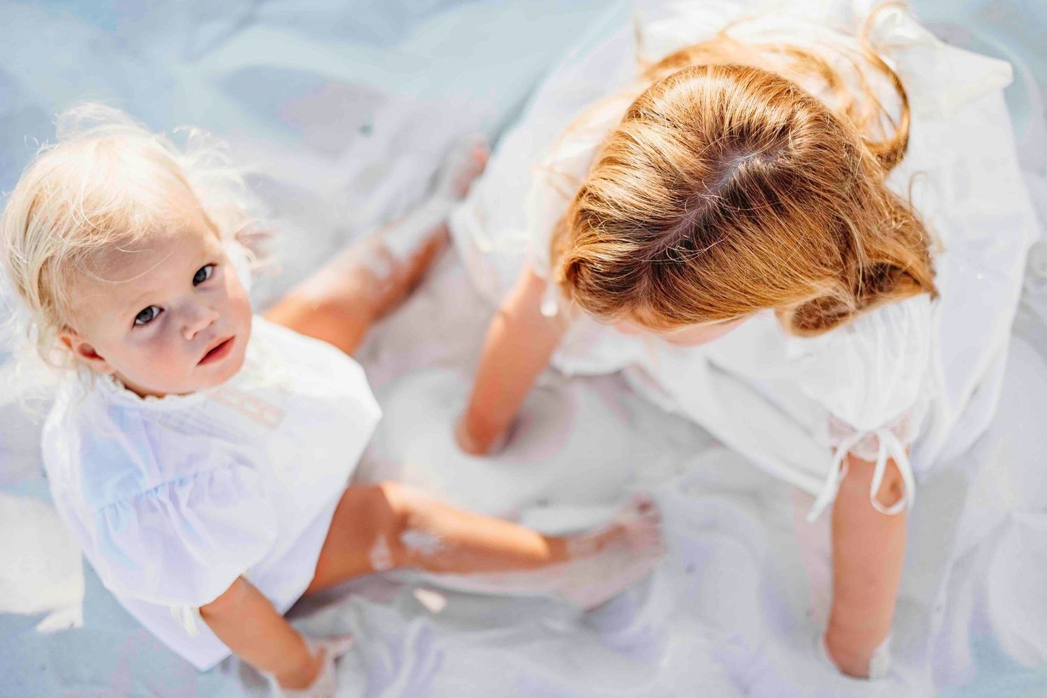 Family members in white clothing share intimate moments on sunny beach.