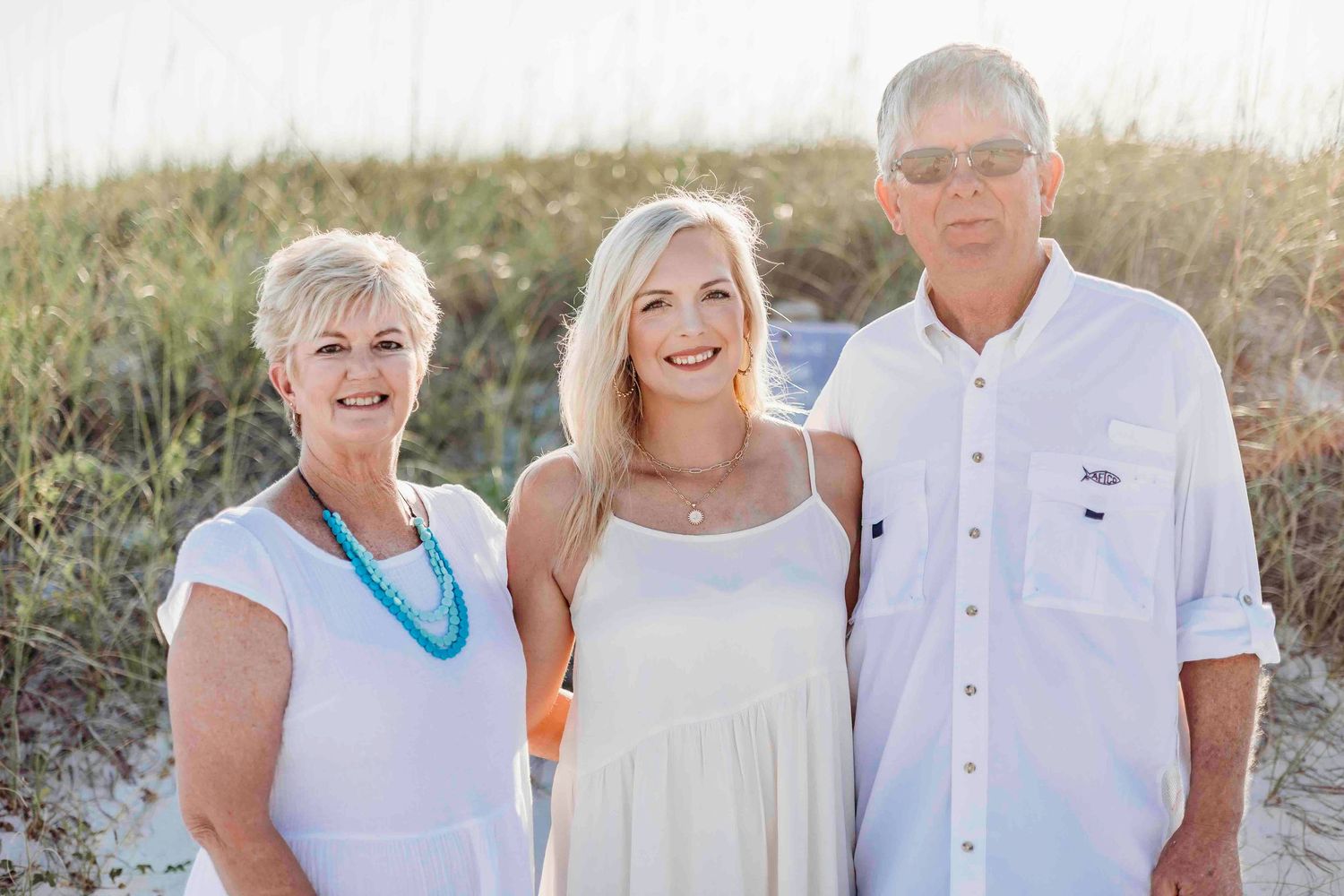 Multi-generational family poses together in white outfits for beach portrait.