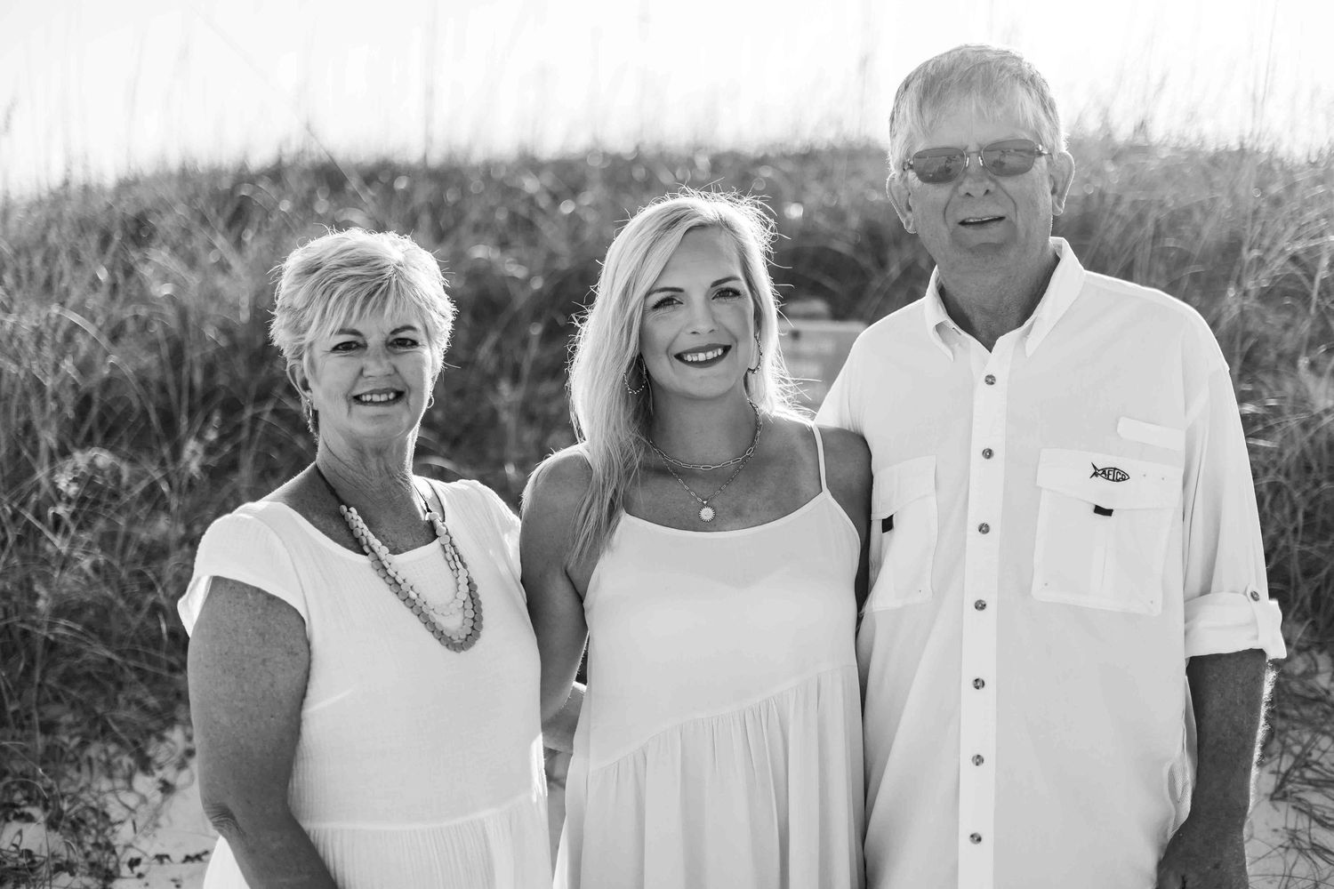 Extended family group wearing coordinated white clothing poses on coastal dunes.