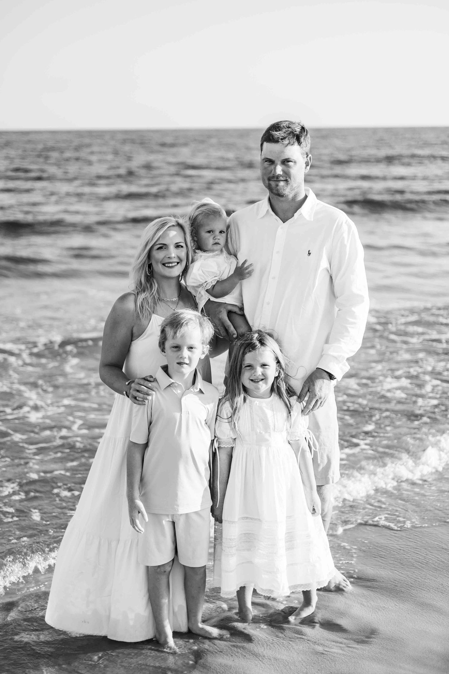 Monochrome family beach portrait with group standing together near ocean waves.