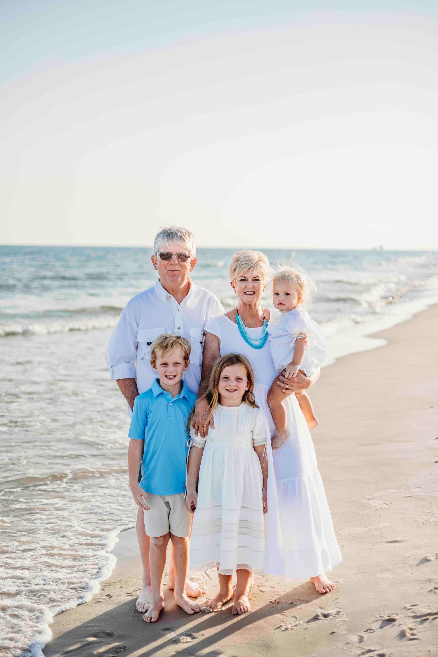 Extended family group poses together on beach with ocean waves in background.