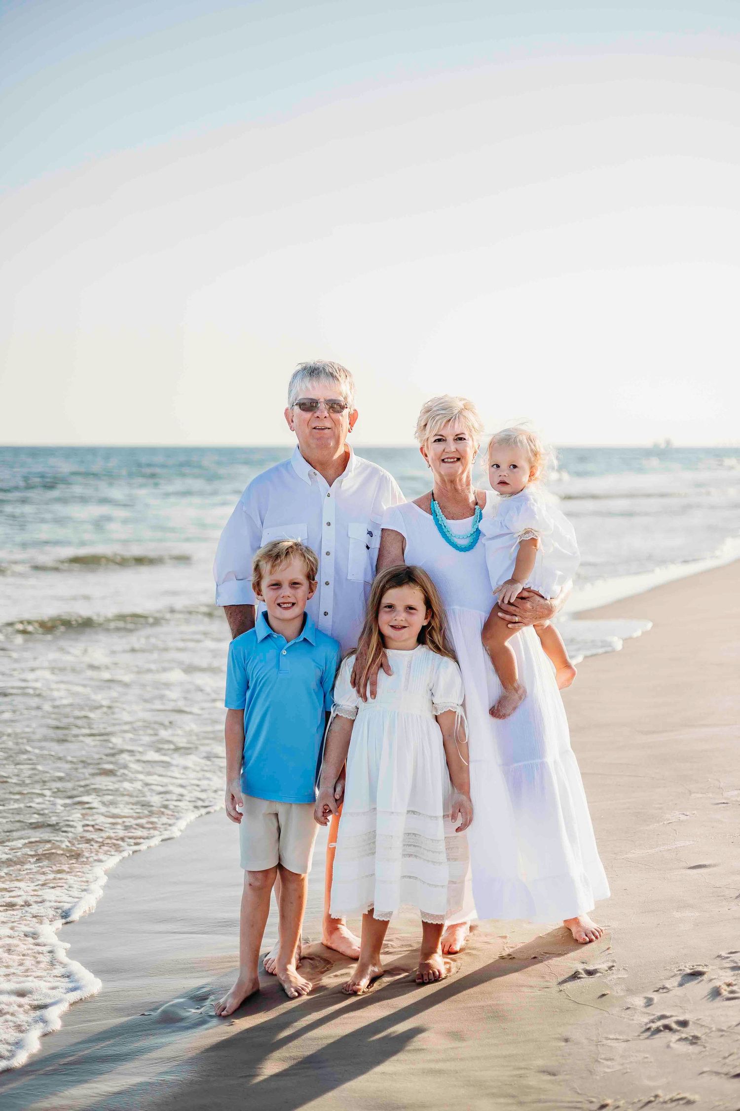 Family group in coordinated outfits poses together on beach at sunset.