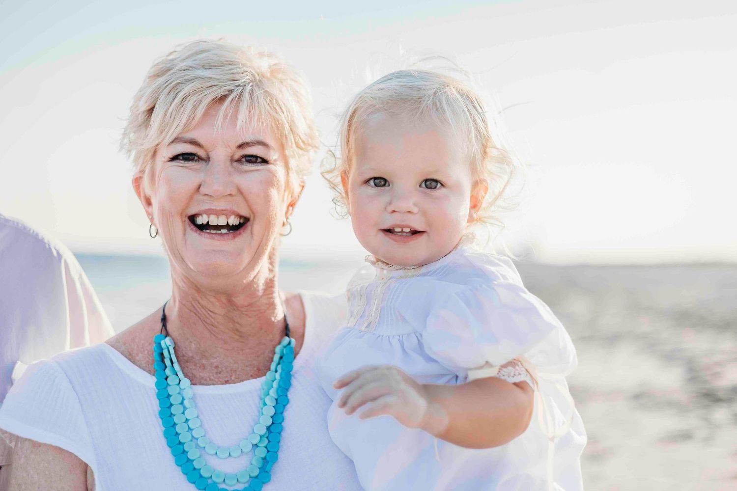 Close-up portrait of two people smiling against beach background.