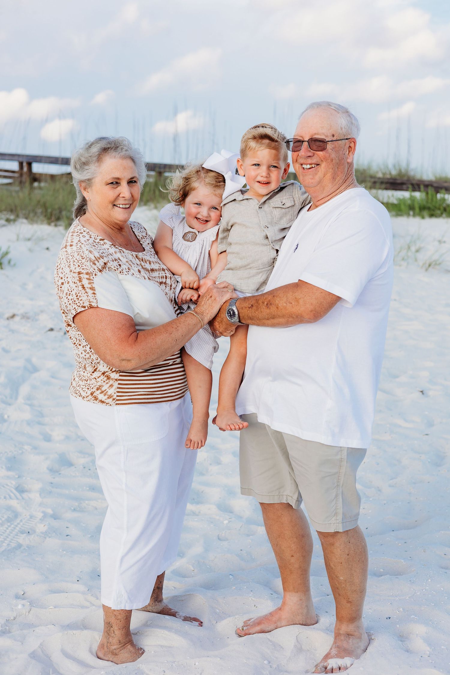 Multi-generational family portrait on beach with sand dunes and wooden fence in background.