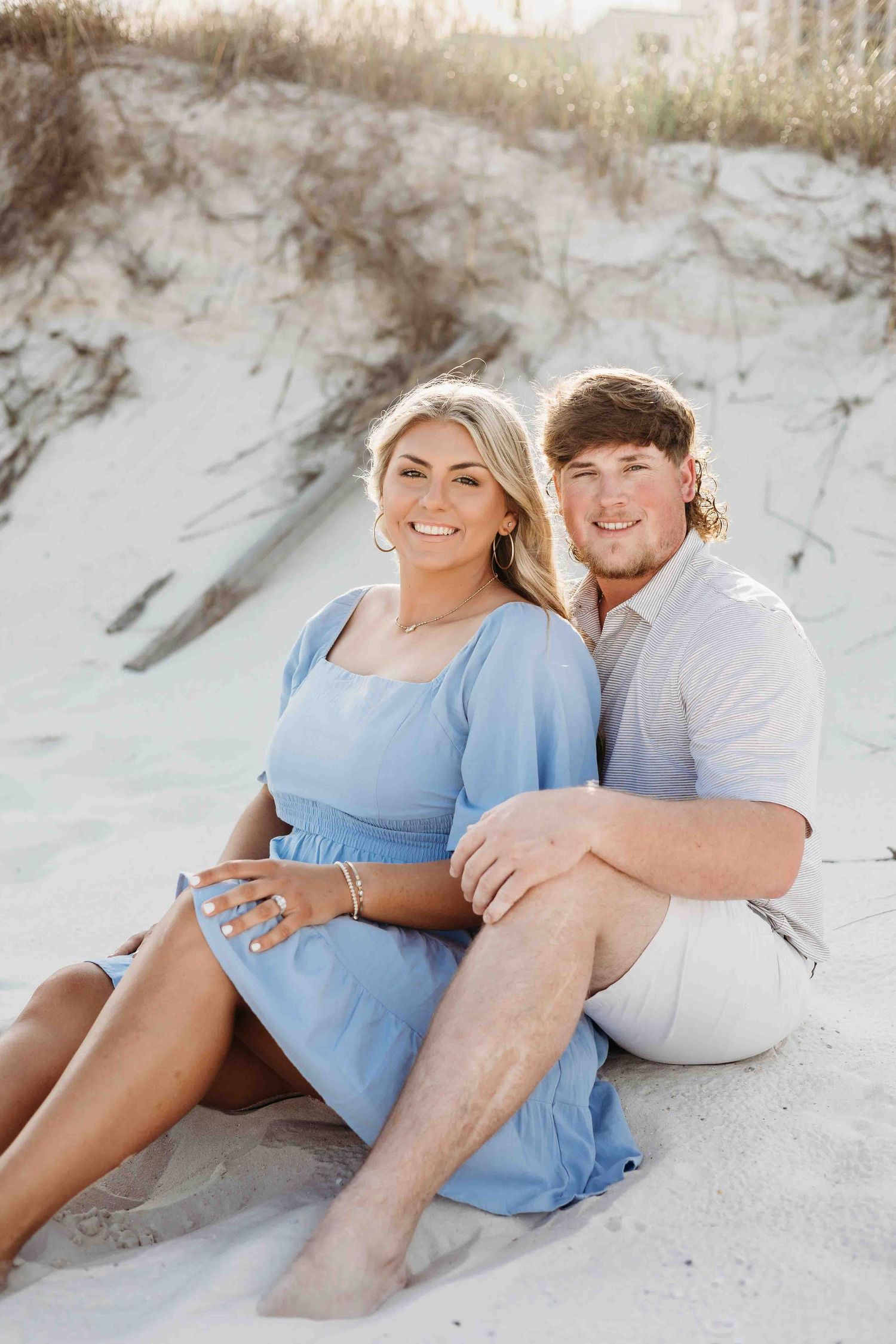 Couple relaxes on sandy dunes wearing coordinating blue and white outfits.