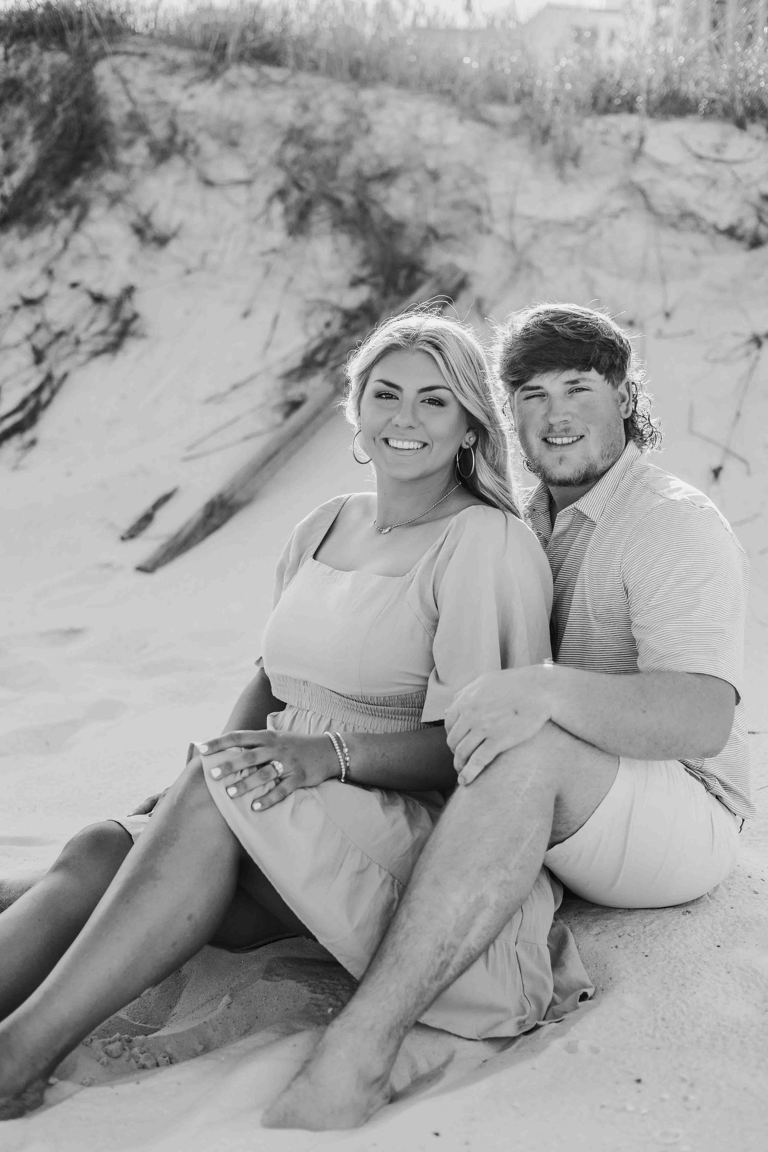 Black and white portrait of couple sharing intimate moment on sandy beach dunes.