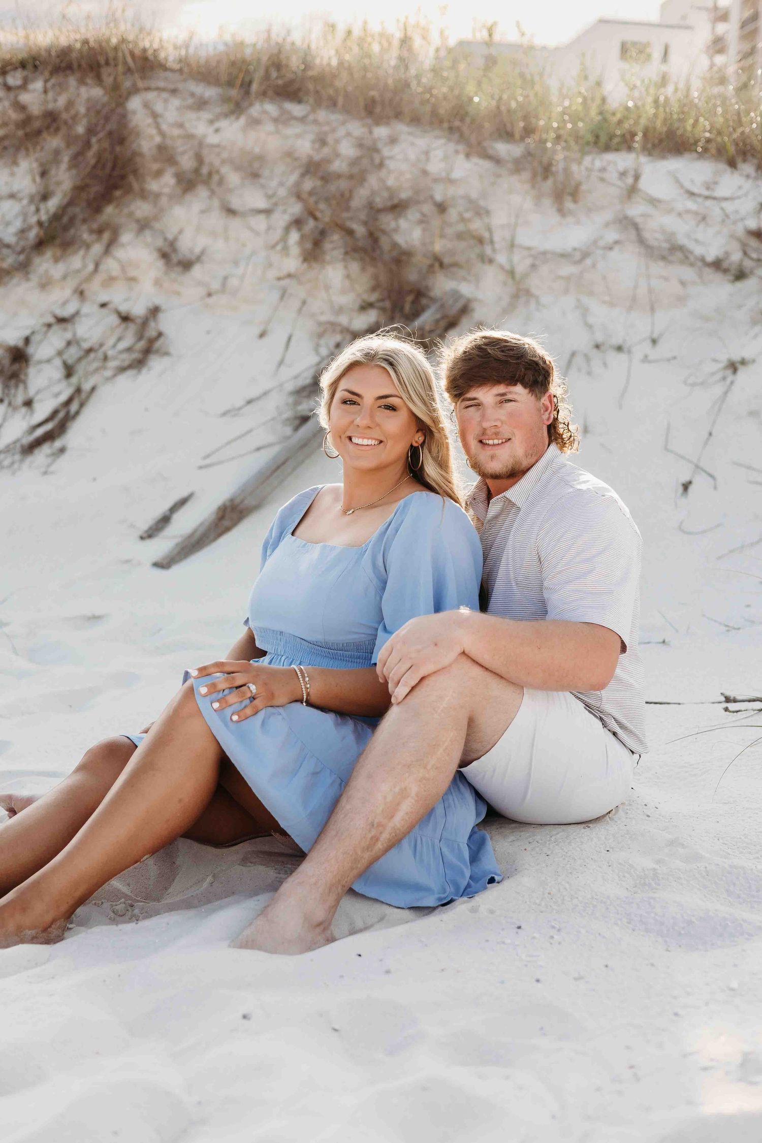 Couple lounges together on white sand beach wearing coordinated casual outfits.