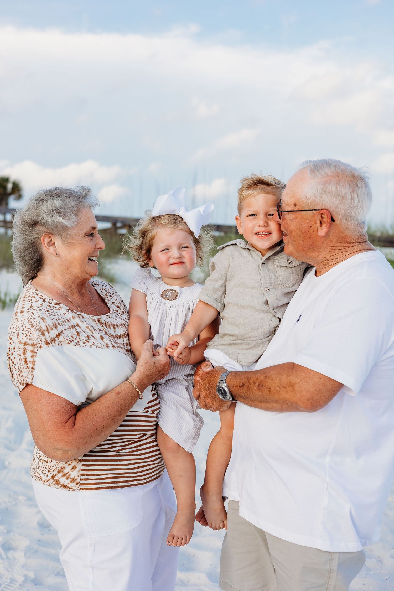 Joyful family moment captured on beach with sand dunes and blue sky in background.