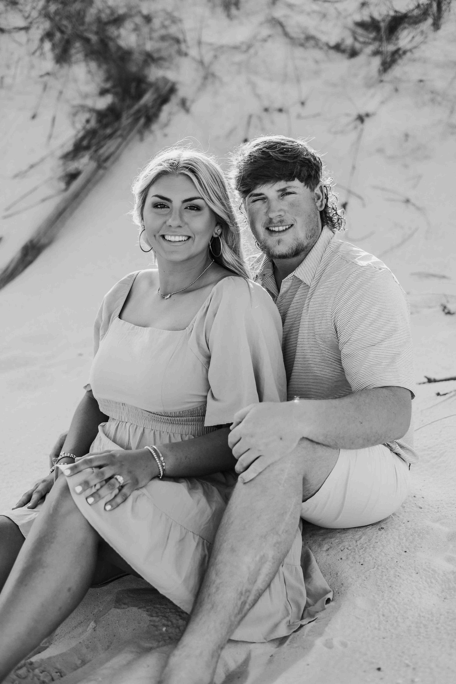 Black and white beach portrait of couple lounging together on sandy dunes.