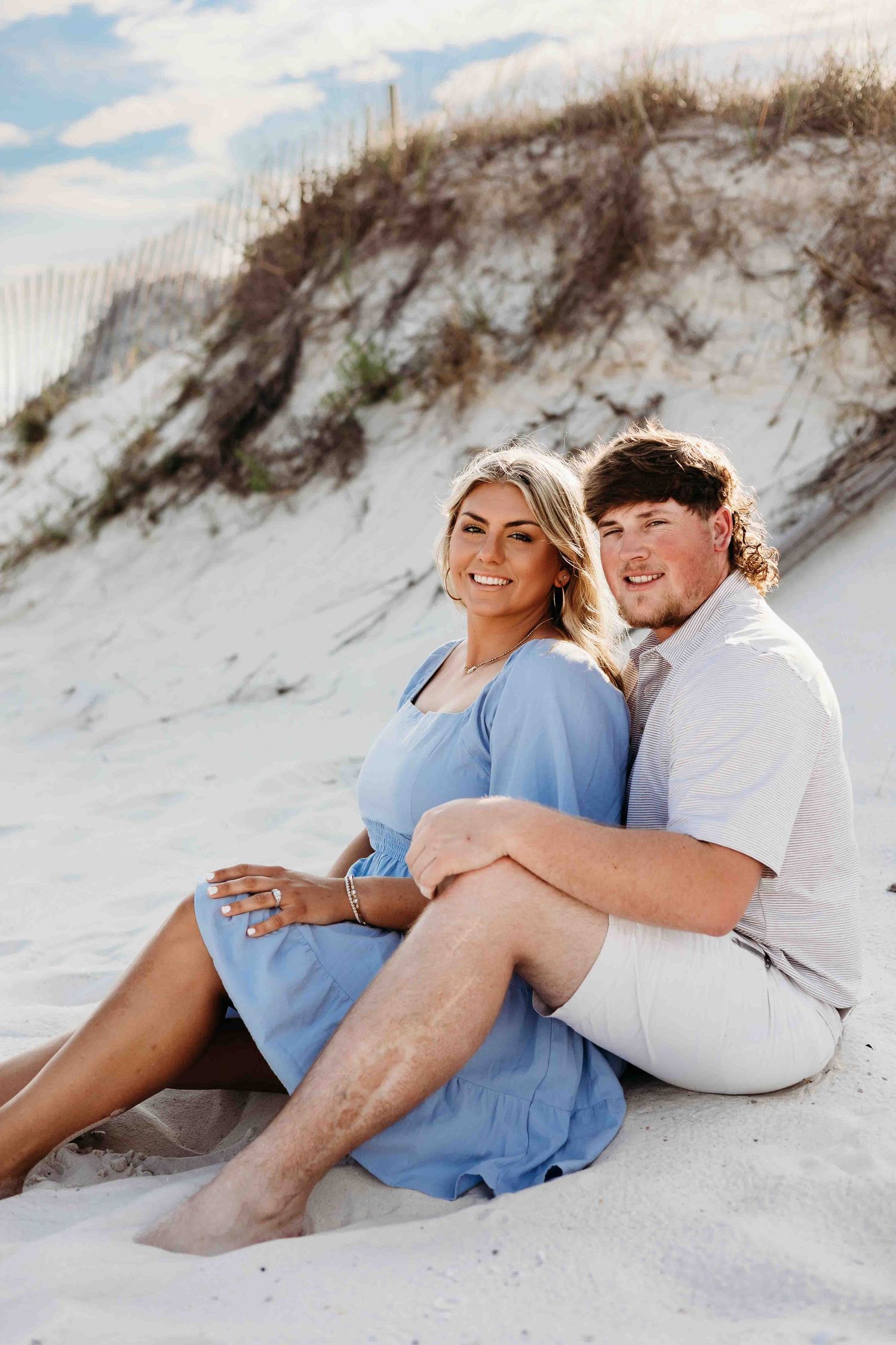 Couple relaxing on sandy dunes during sunset beach photoshoot.
