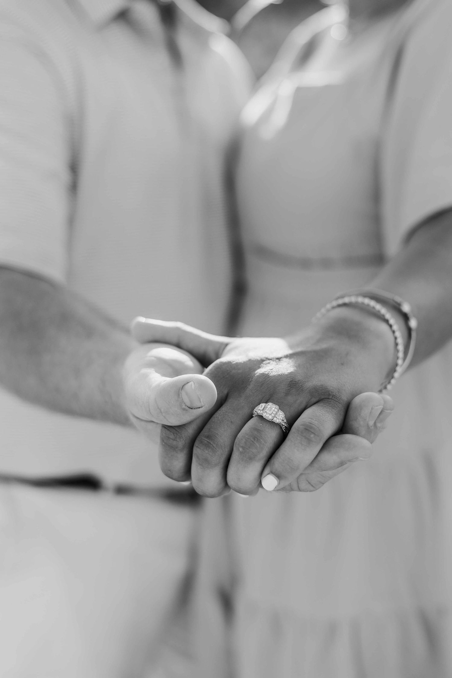 Black and white detail shot of hands displaying engagement ring.