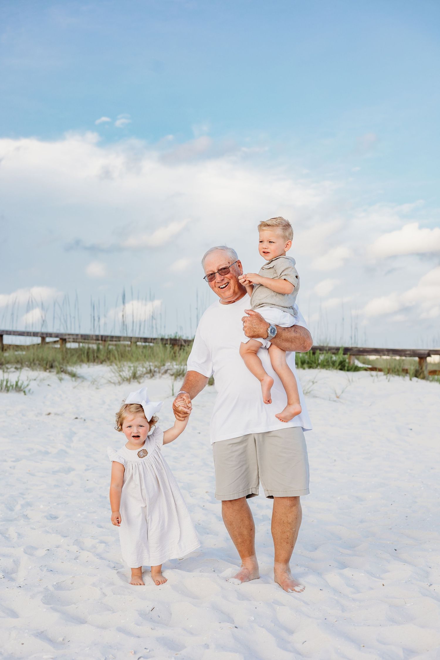 Family members playing and running on white sandy beach under blue skies.