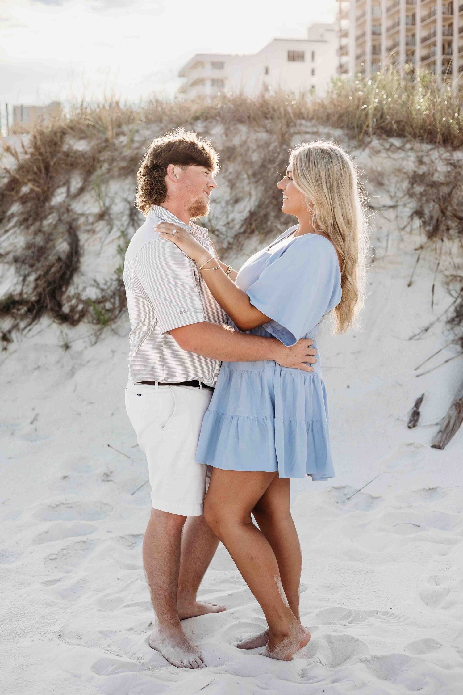 Two people pose playfully in the sand during a beachside photoshoot.