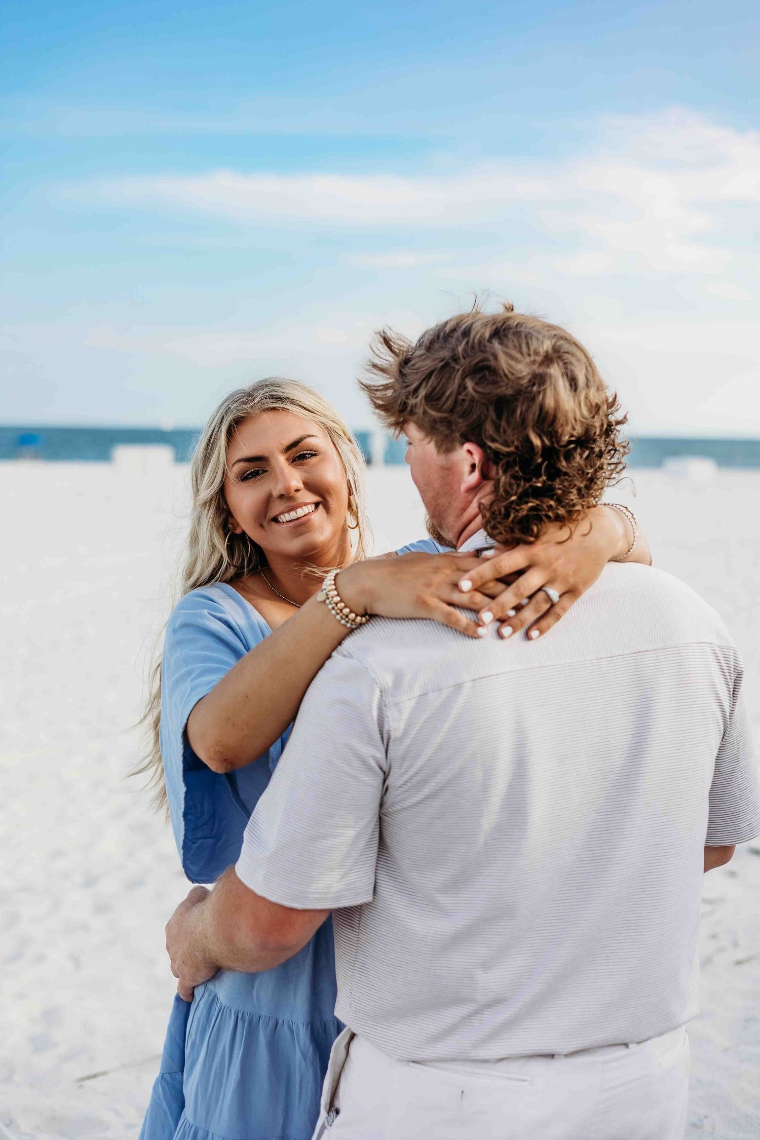 Romantic beach proposal moment between couple on white sandy beach with blue sky.