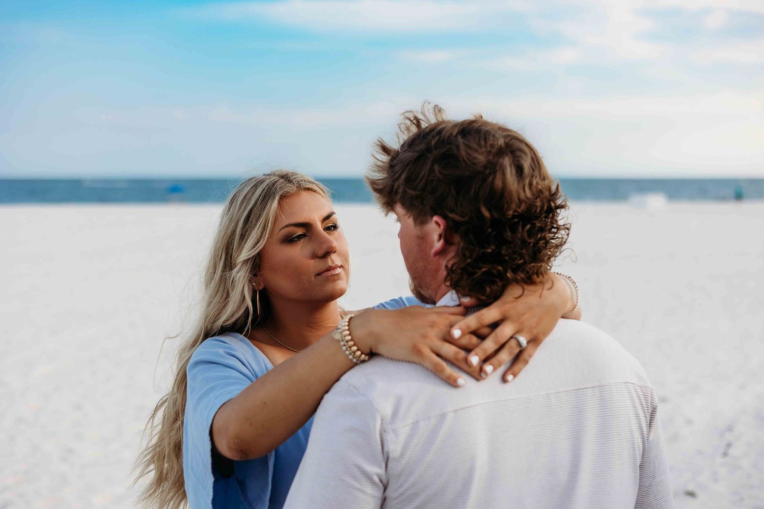 Couple sharing intimate moment on pristine white beach with ocean backdrop.