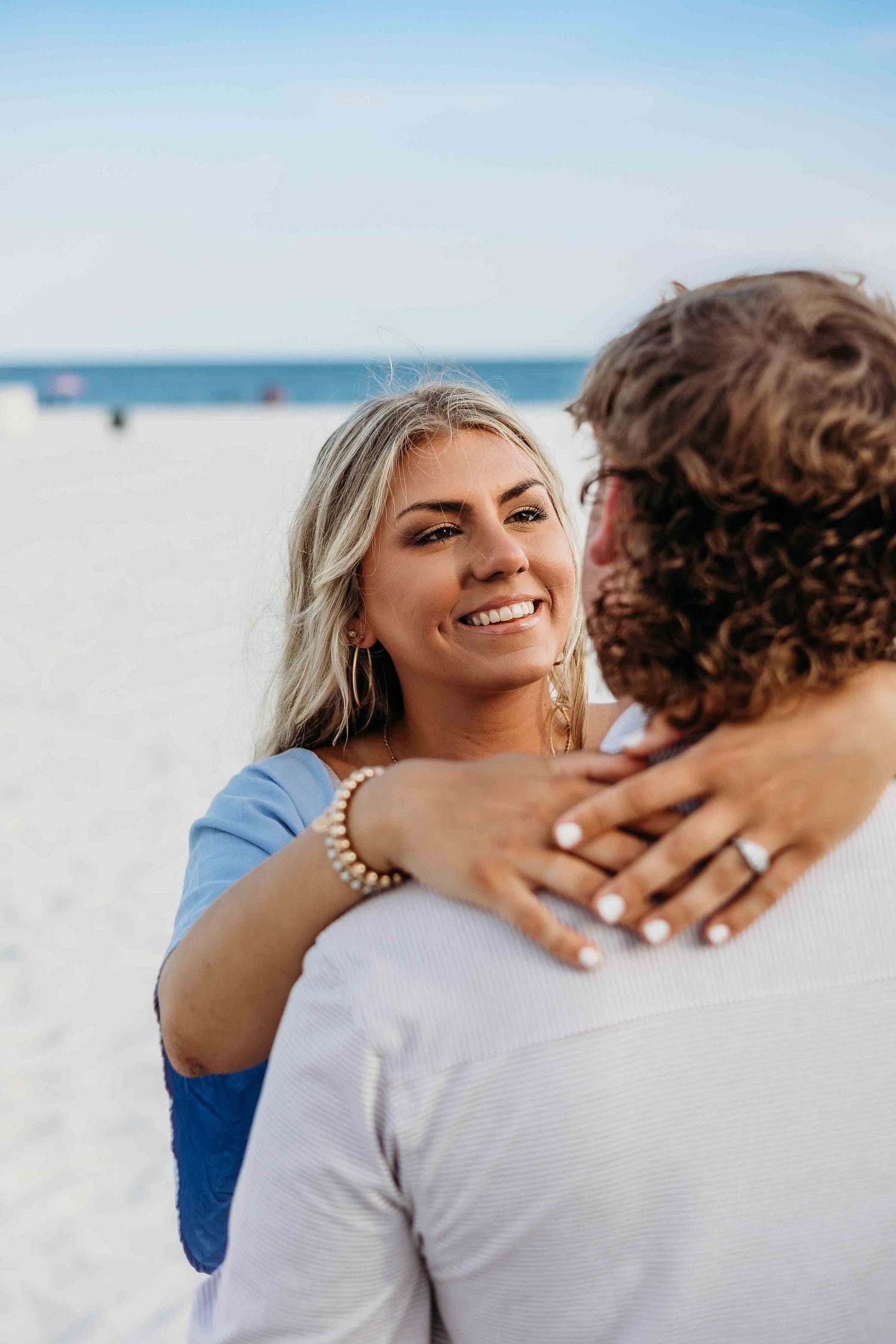 Happy couple embracing on sunny beach after proposal moment.